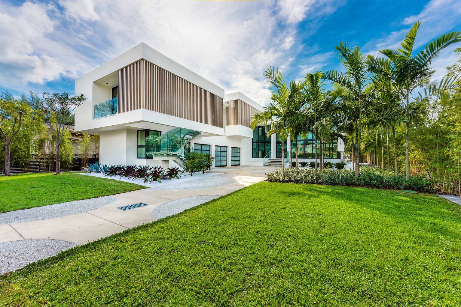 A modern build in miami beach with a large front yard and palm trees throughout.