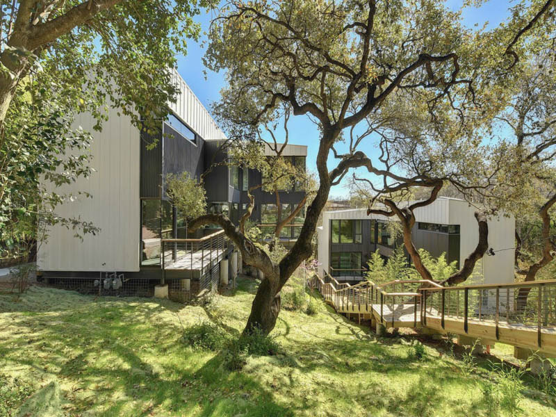A green, sloping lot with willowy trees and a contemporary white-stucco-and-metal building