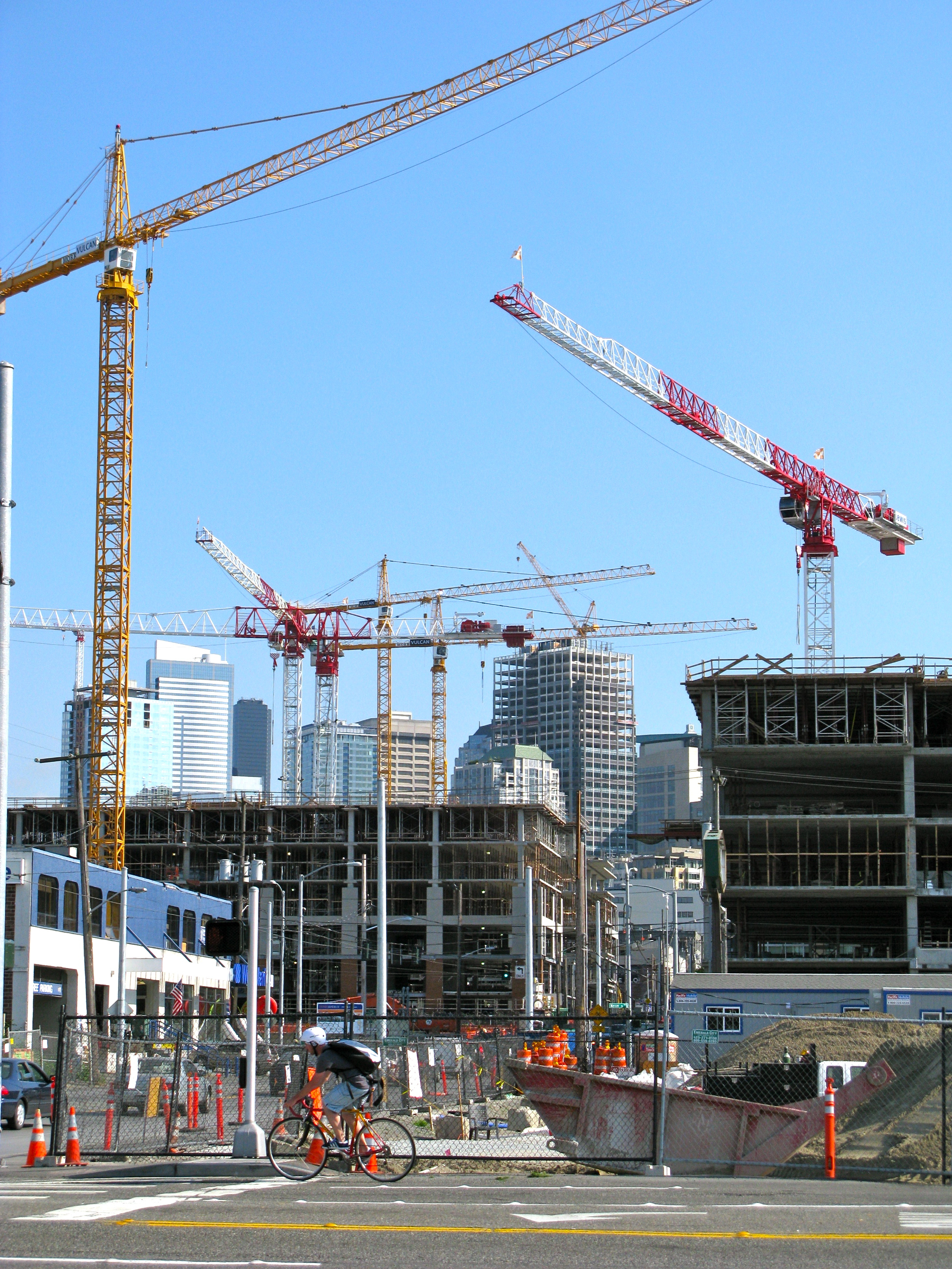 A number of cranes over buildings, with a view of Downtown Seattle