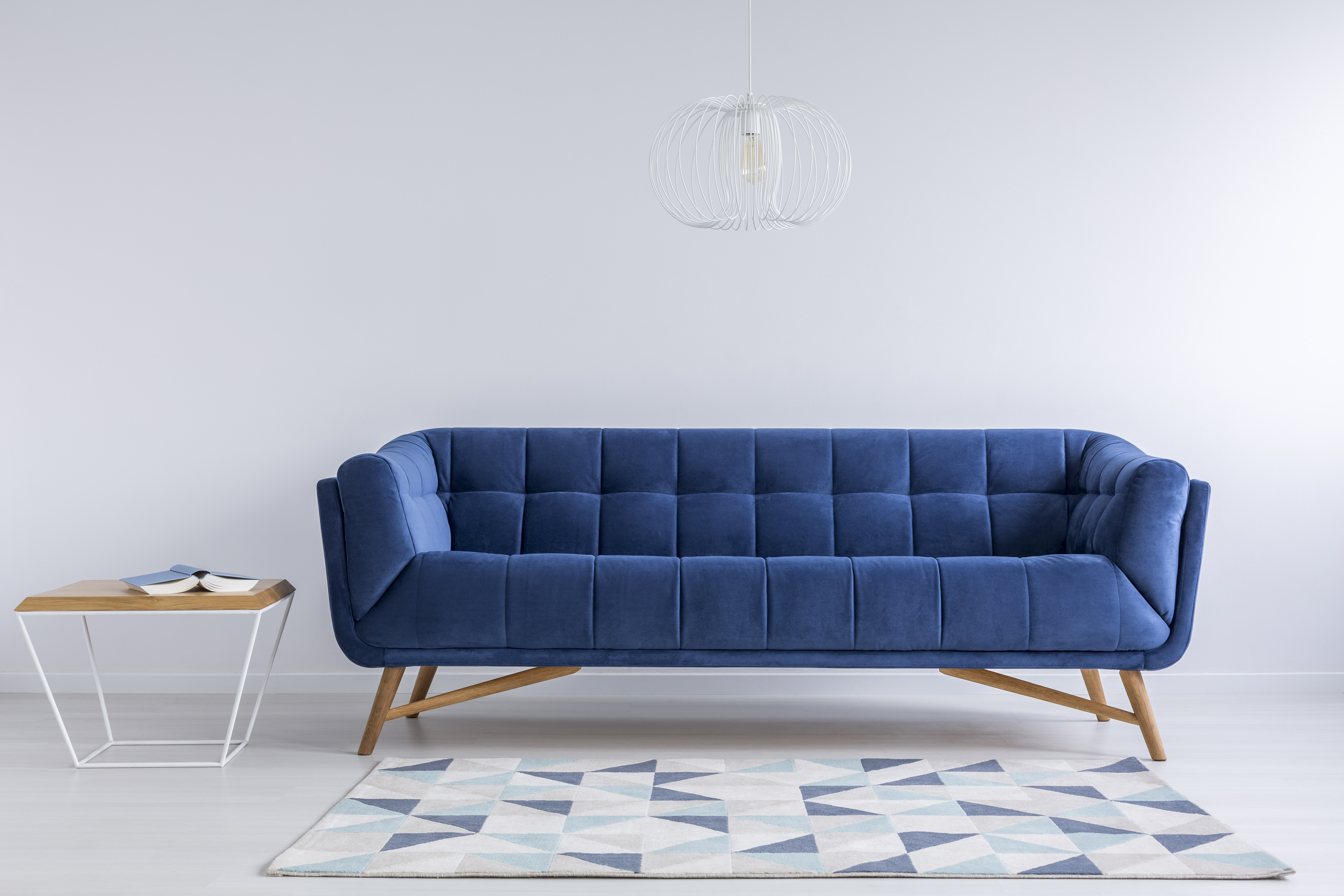 白色的房间里有一张宝蓝色的沙发，沙发脚边有一张带图案的地毯，沙发左边有一张现代的小桌子。