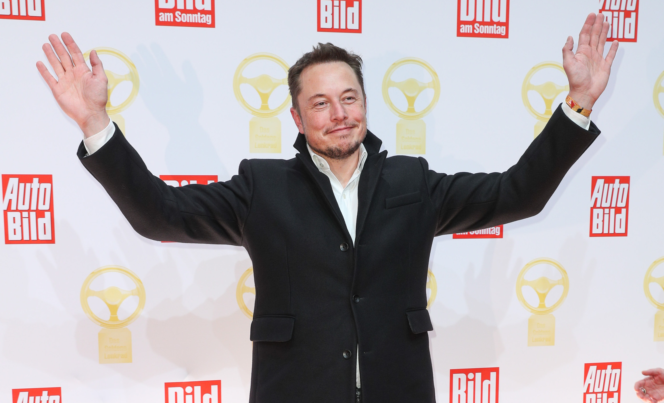 Elon Musk poses with his arms raised.