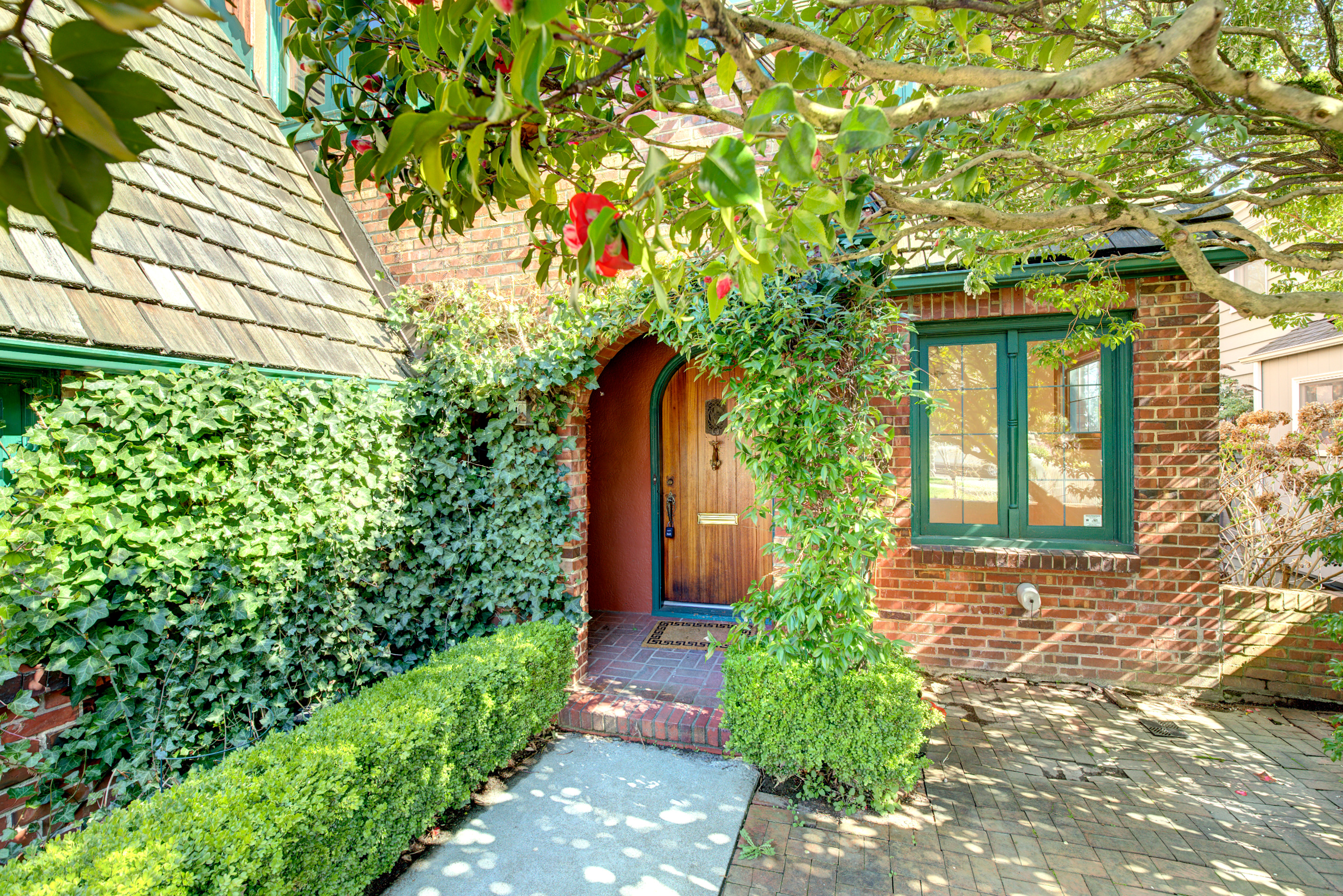 The front walkway of a brick house with green trim is covered in ivy