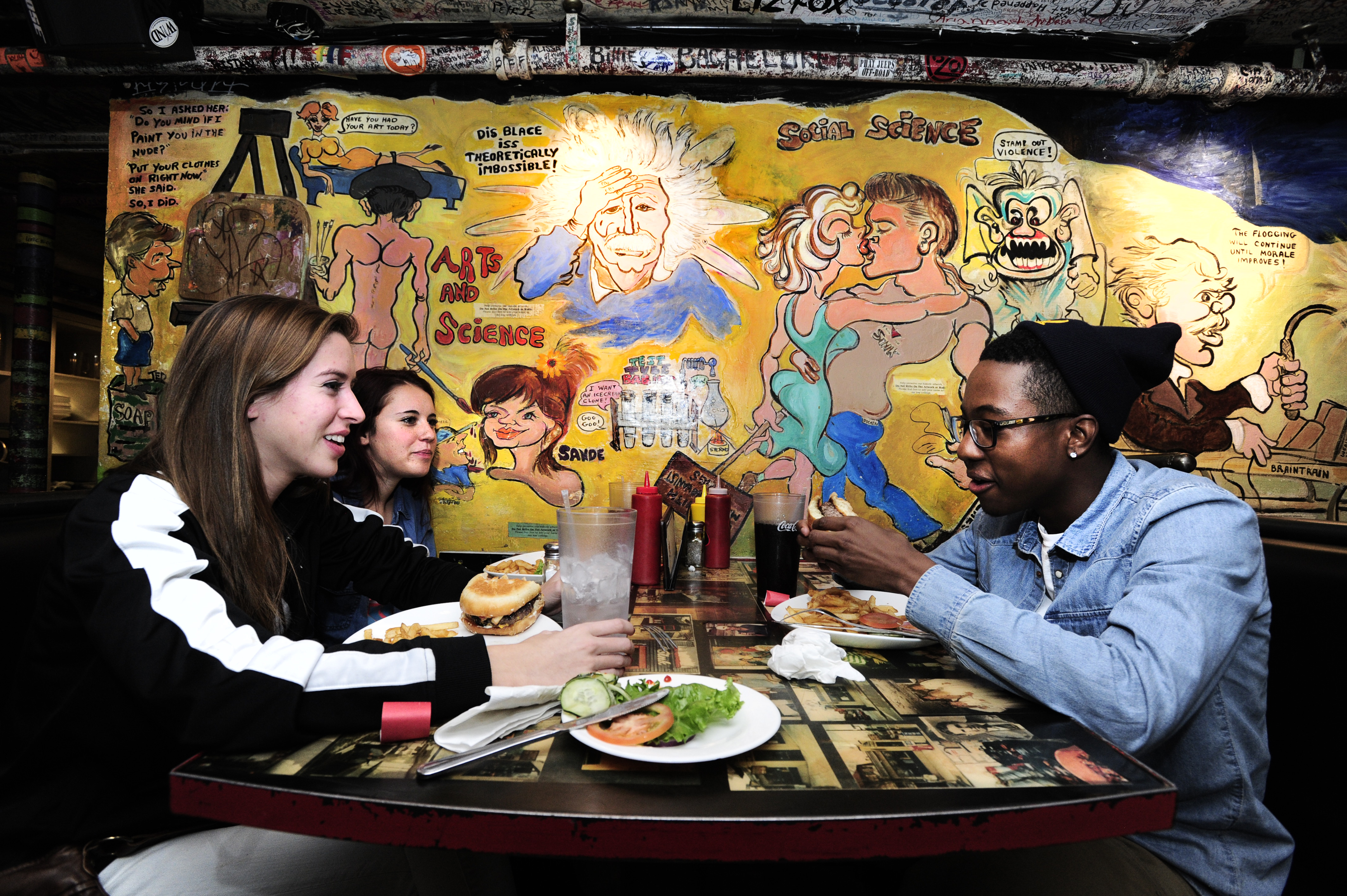 Three customers enjoy a meal in front of a large cartoon mural covering the wall.