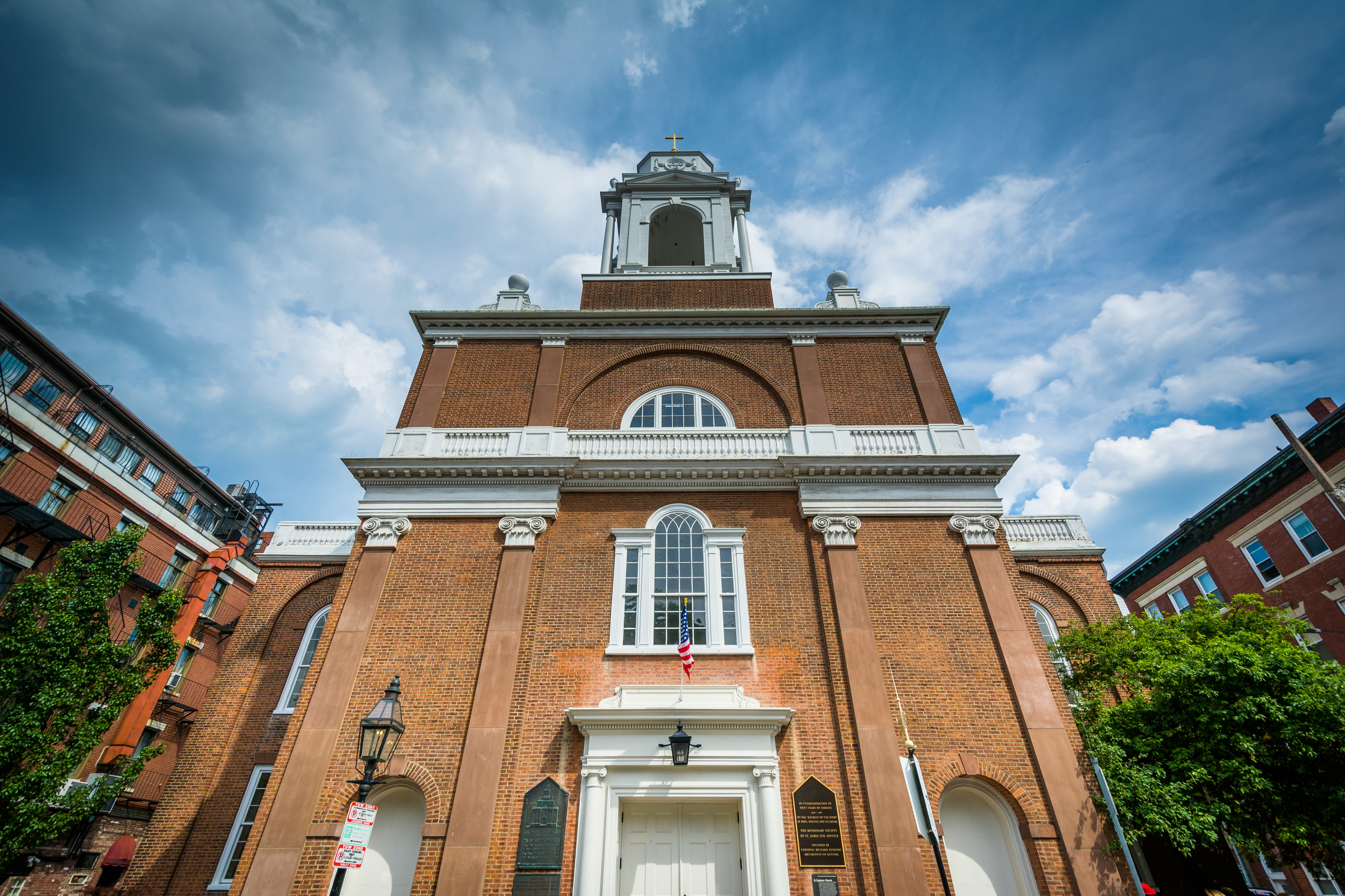 The exterior of three-story, thin, brick building ending in a thinner steeple.