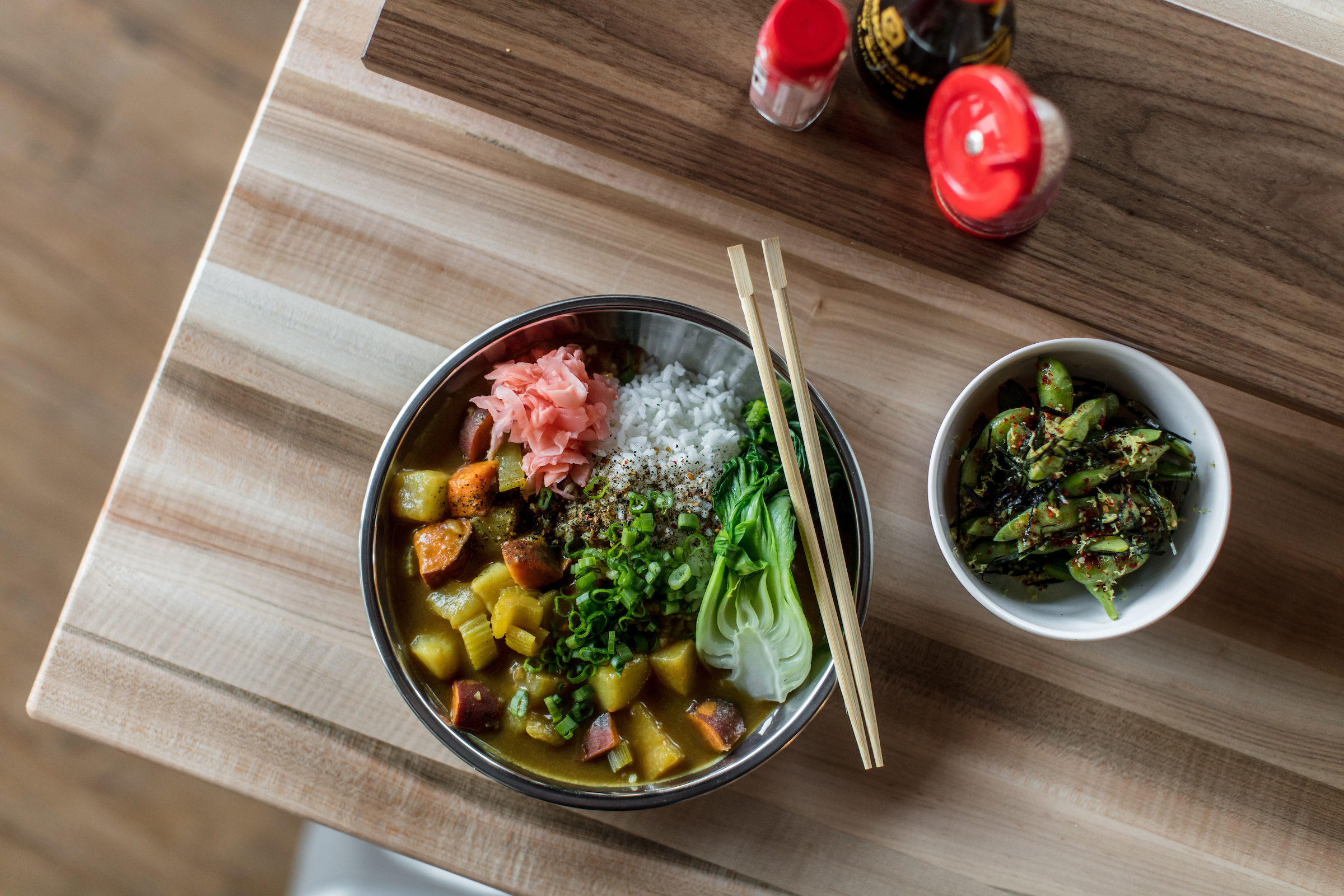 A bowl of golden curry and rice with bok choy and veggies with a side of edamame. 