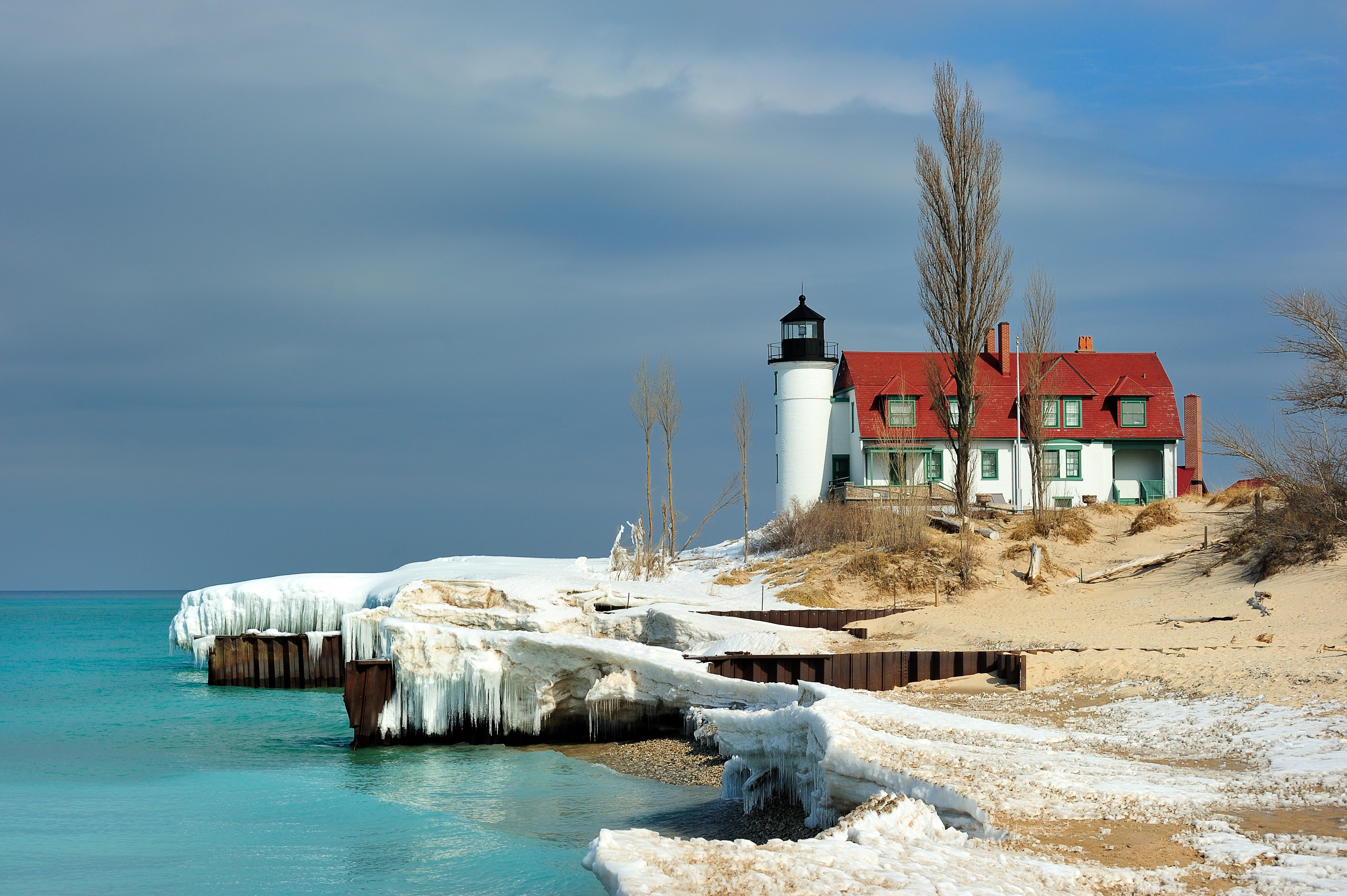 A lighthouse and barn next to a lake with an icy shore.