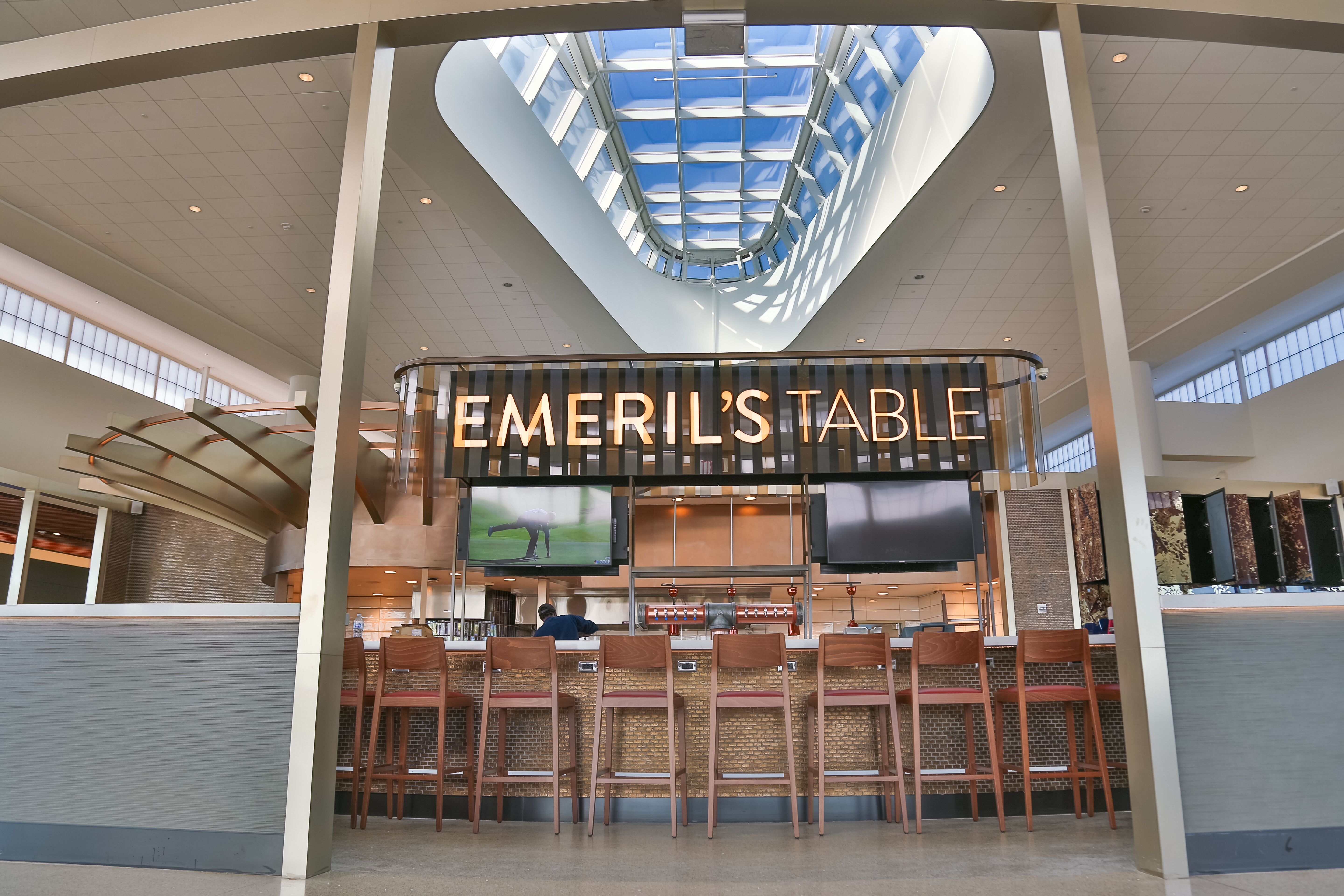 A long bar with an “Emeril’s Table” sign hanging above sits under a large skylight at the New Orleans airport.