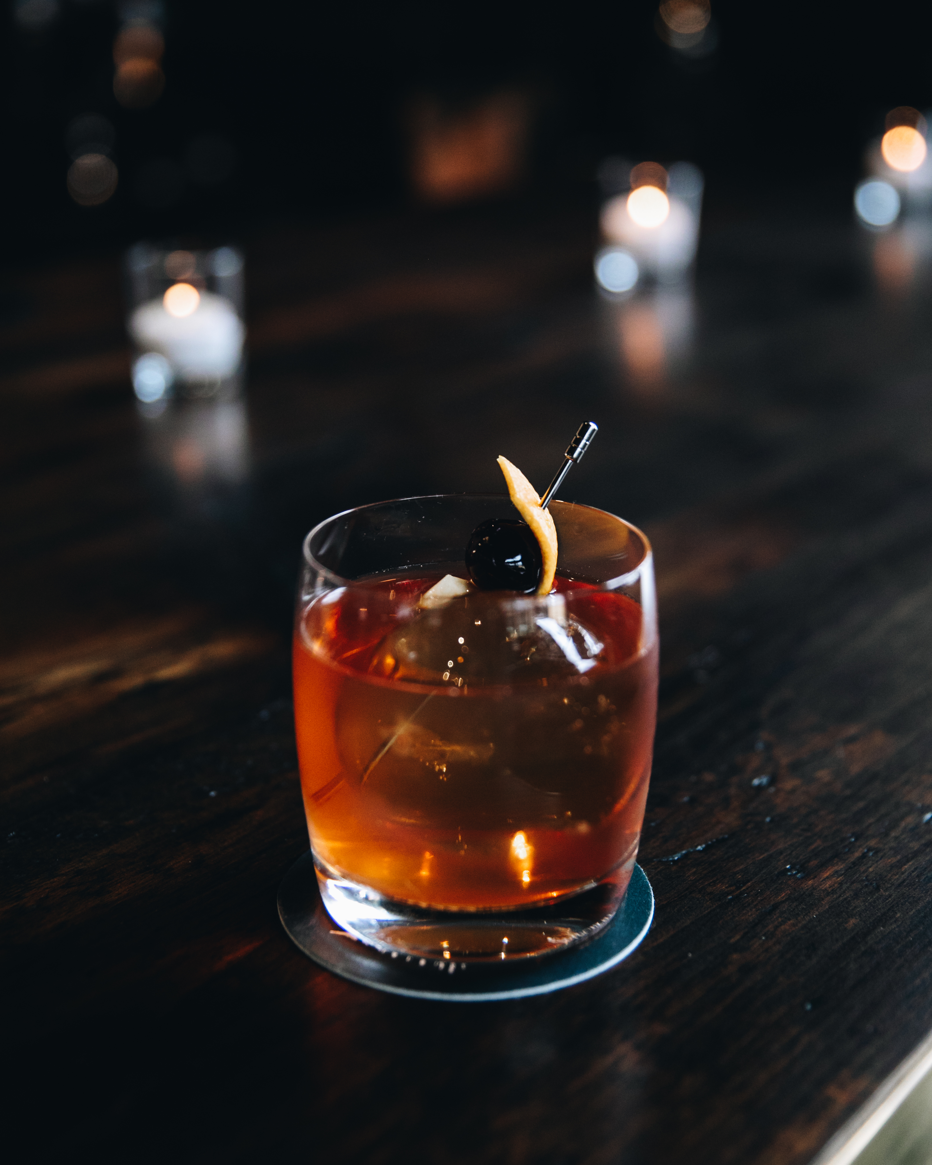 An Old Fashioned sitting on a dark wood bar.