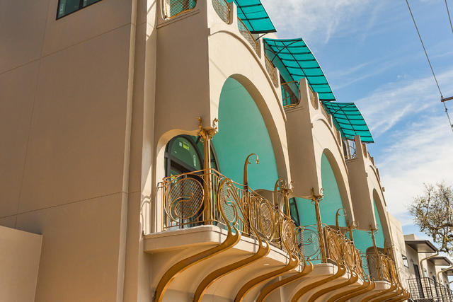 three arched balconies on second floor of stucco building, aqua ceilings, curvy gold railings