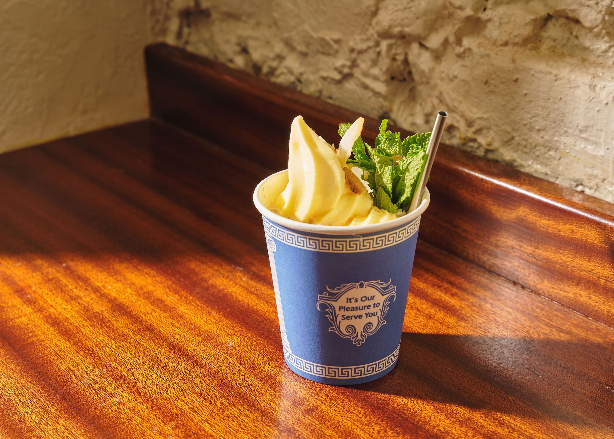 A blue and white plastic coffee cup holding a yellow soft serve with sprigs of mint and a straw.