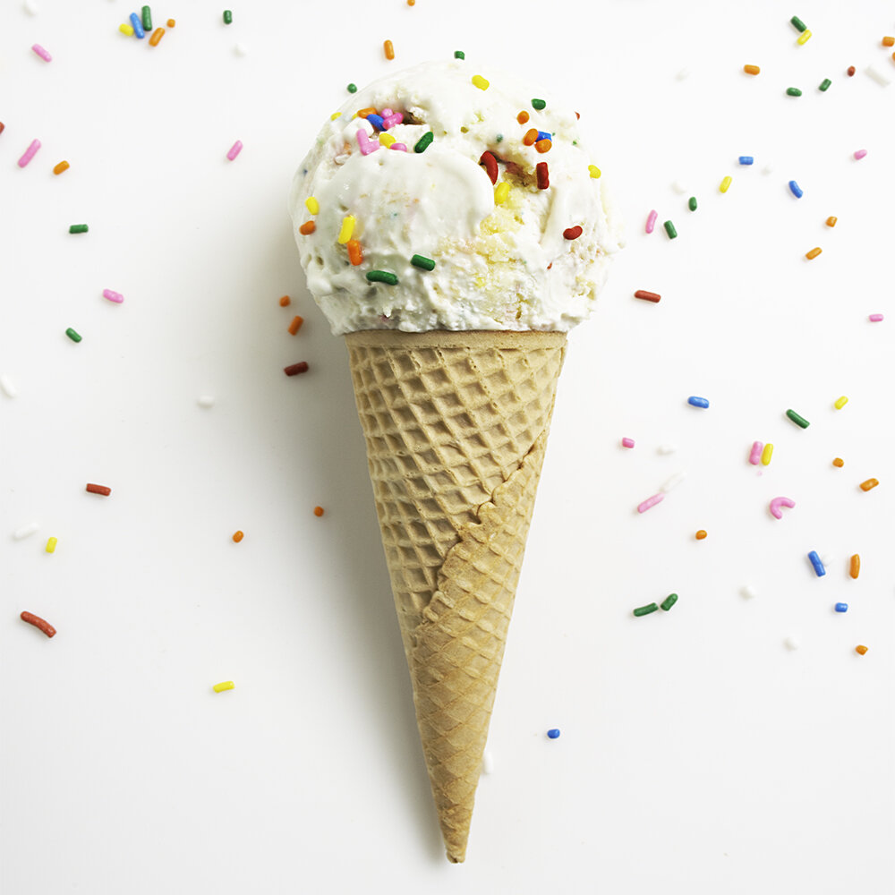 A scoop of ice cream in a cone with sprinkles on a white background with sprinkles.