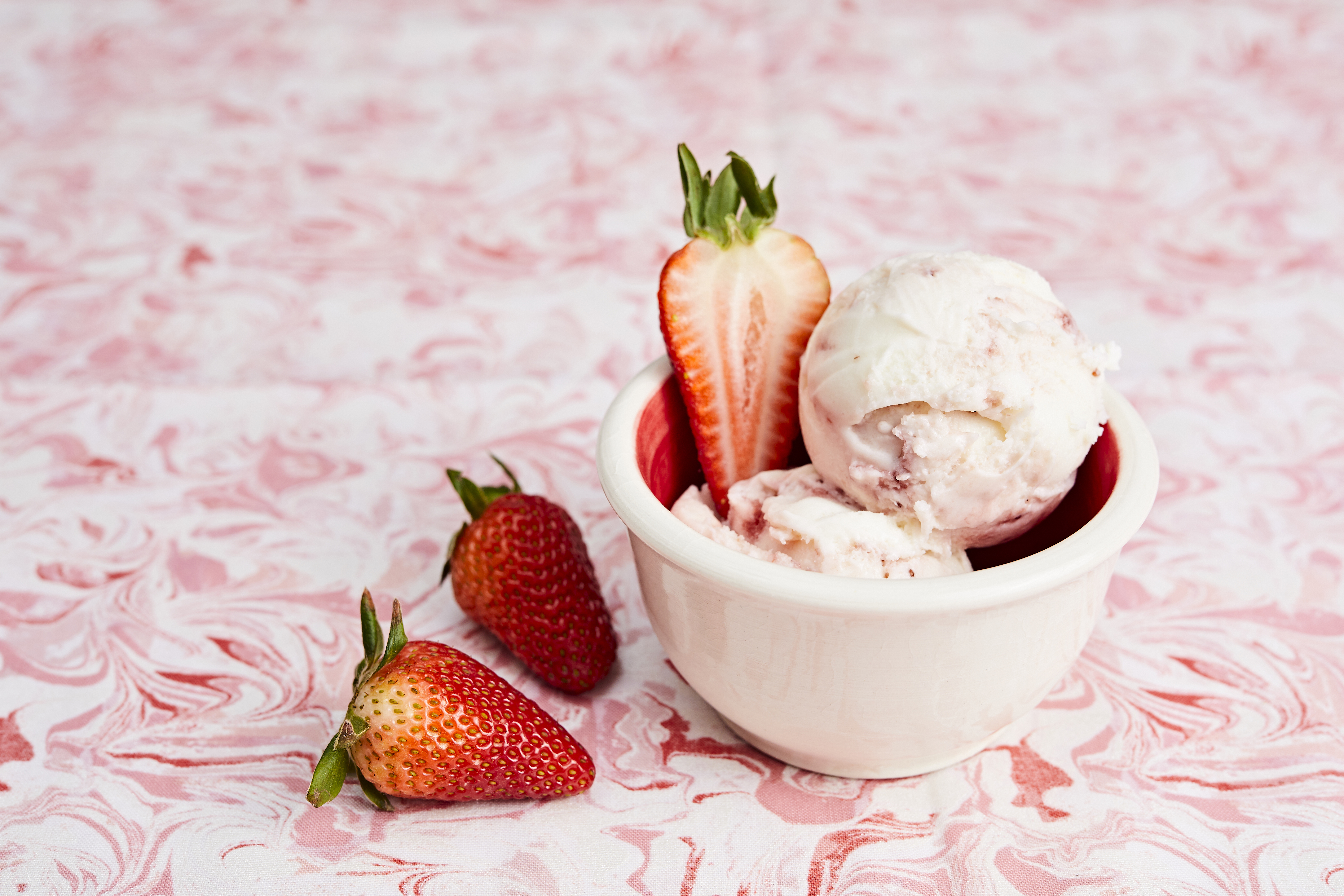 A white bowl of pale-pink ice cream scoops with slices of strawberries.