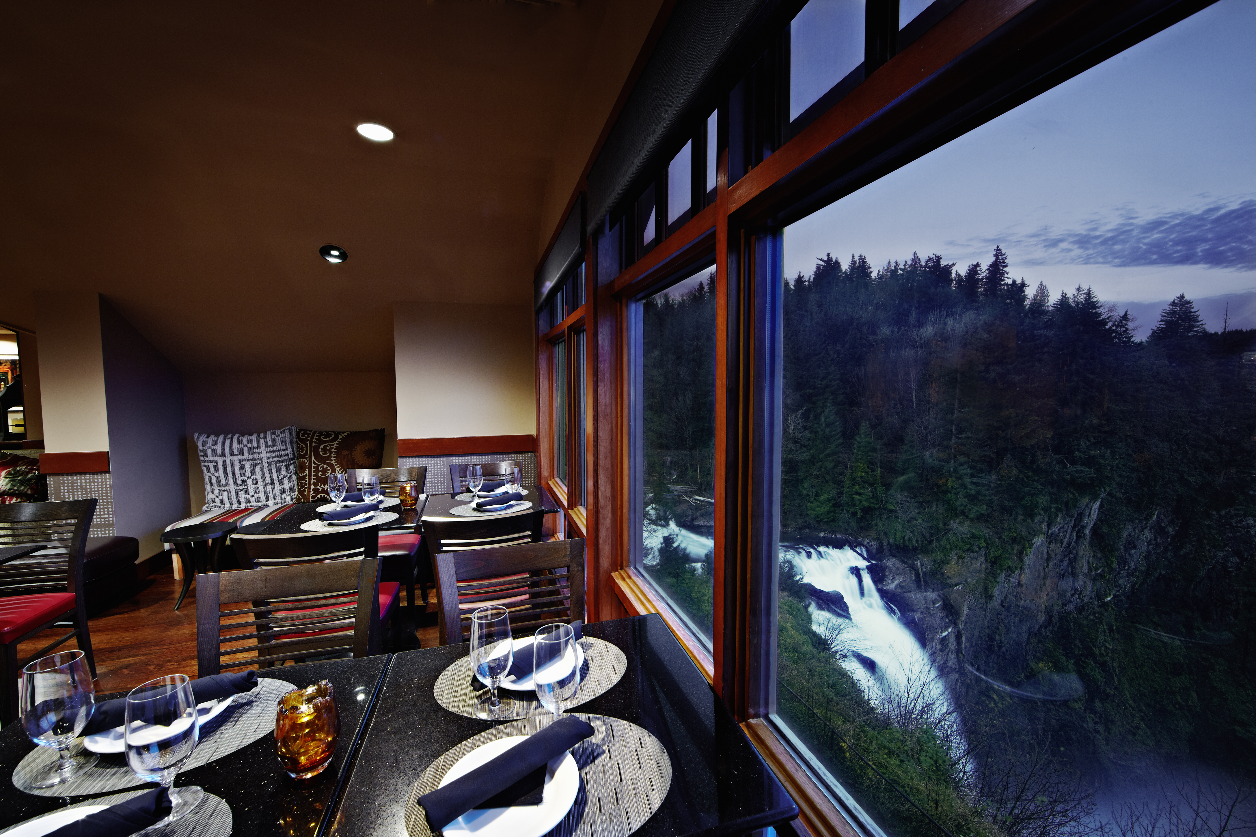 Tables are set with plates and cutlery. A waterfall can be seen through the large windows to the right. 
