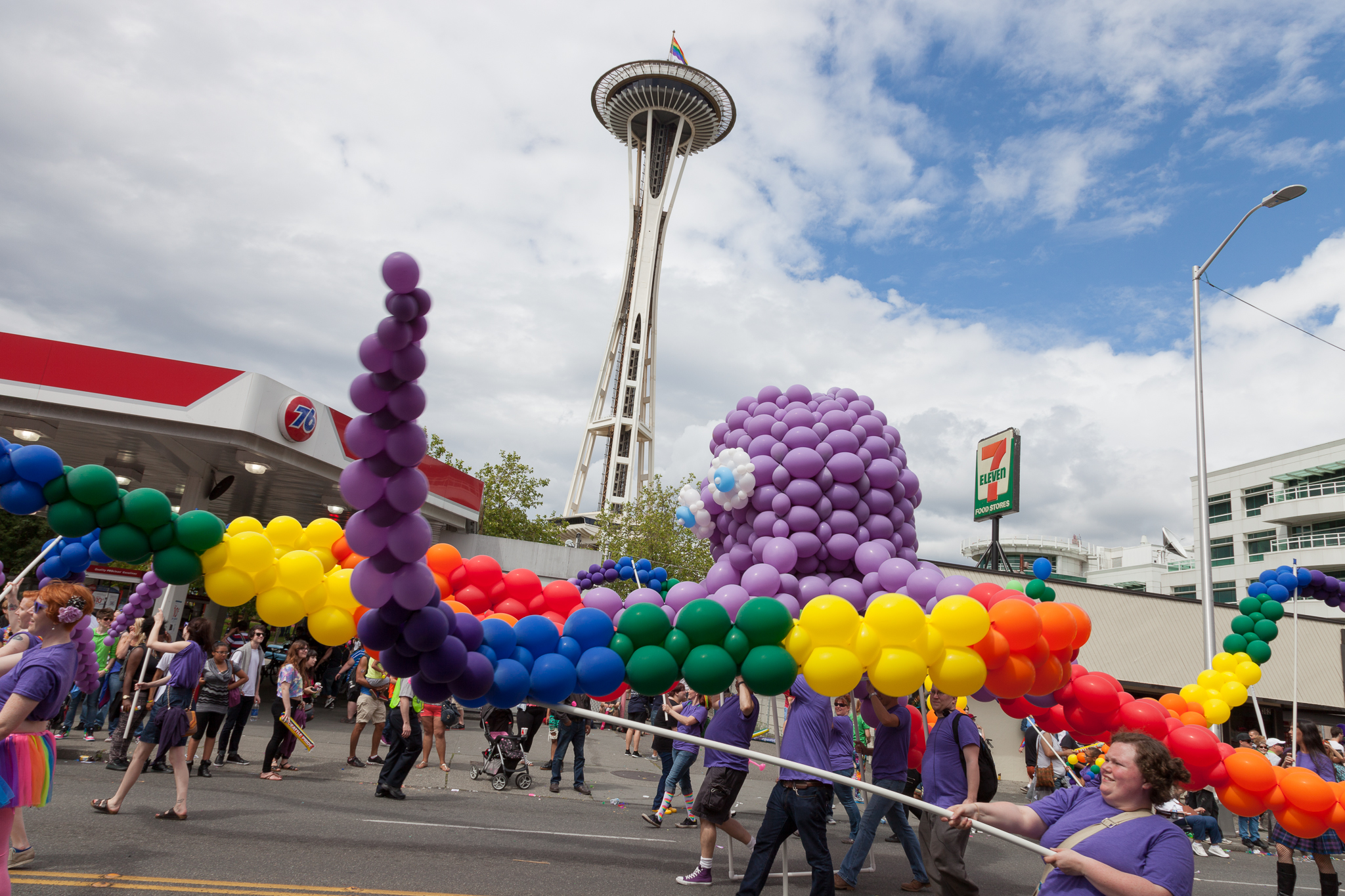 A group of people carrying a giant octopus made out of purple, blue, green yellow, orange, and red balloons with the Space Needle in the background.