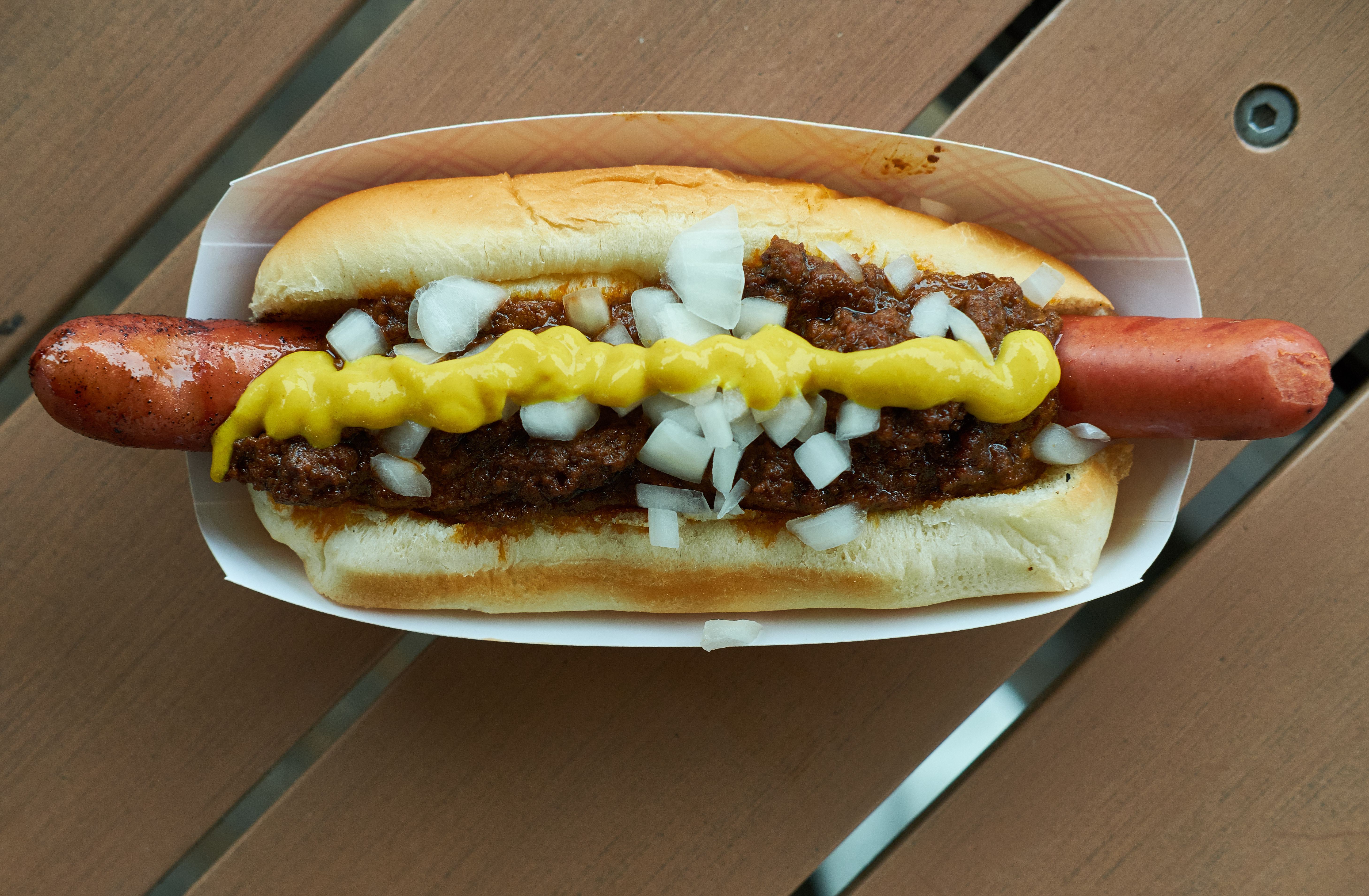 A frankfurter in a bun, covered in Coney sauce, chopped white onion, and yellow mustard.