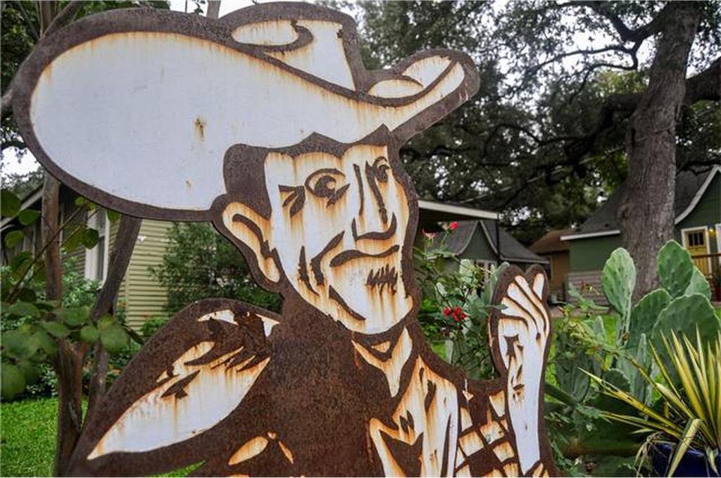 Weathered metal sign of a cowboy with thumb pointing at foliage