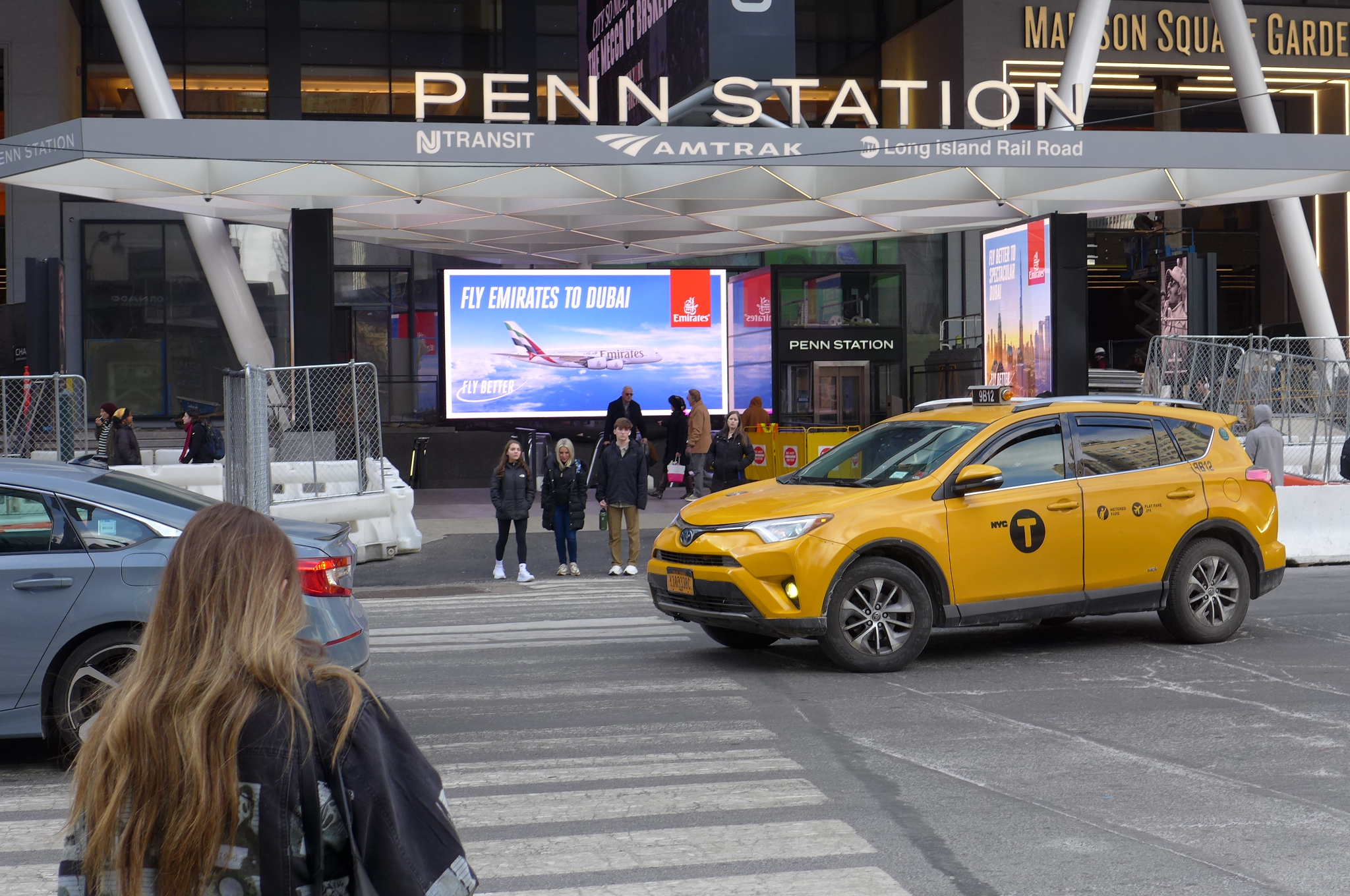 A yellow cab, a few pedestrians, and the 7th Avenue entrance to Penn Station.