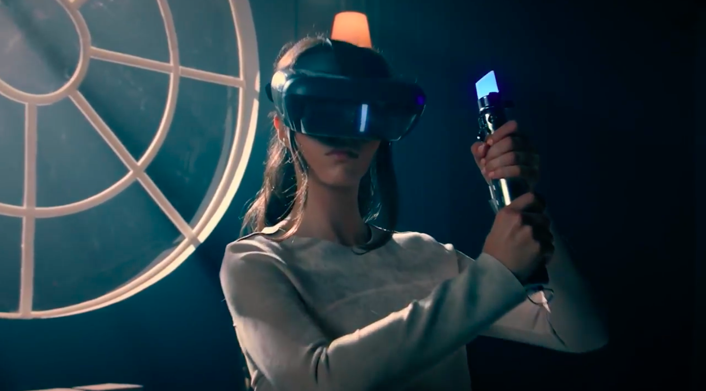 A woman wearing an AR headset holds a lightsaber controller