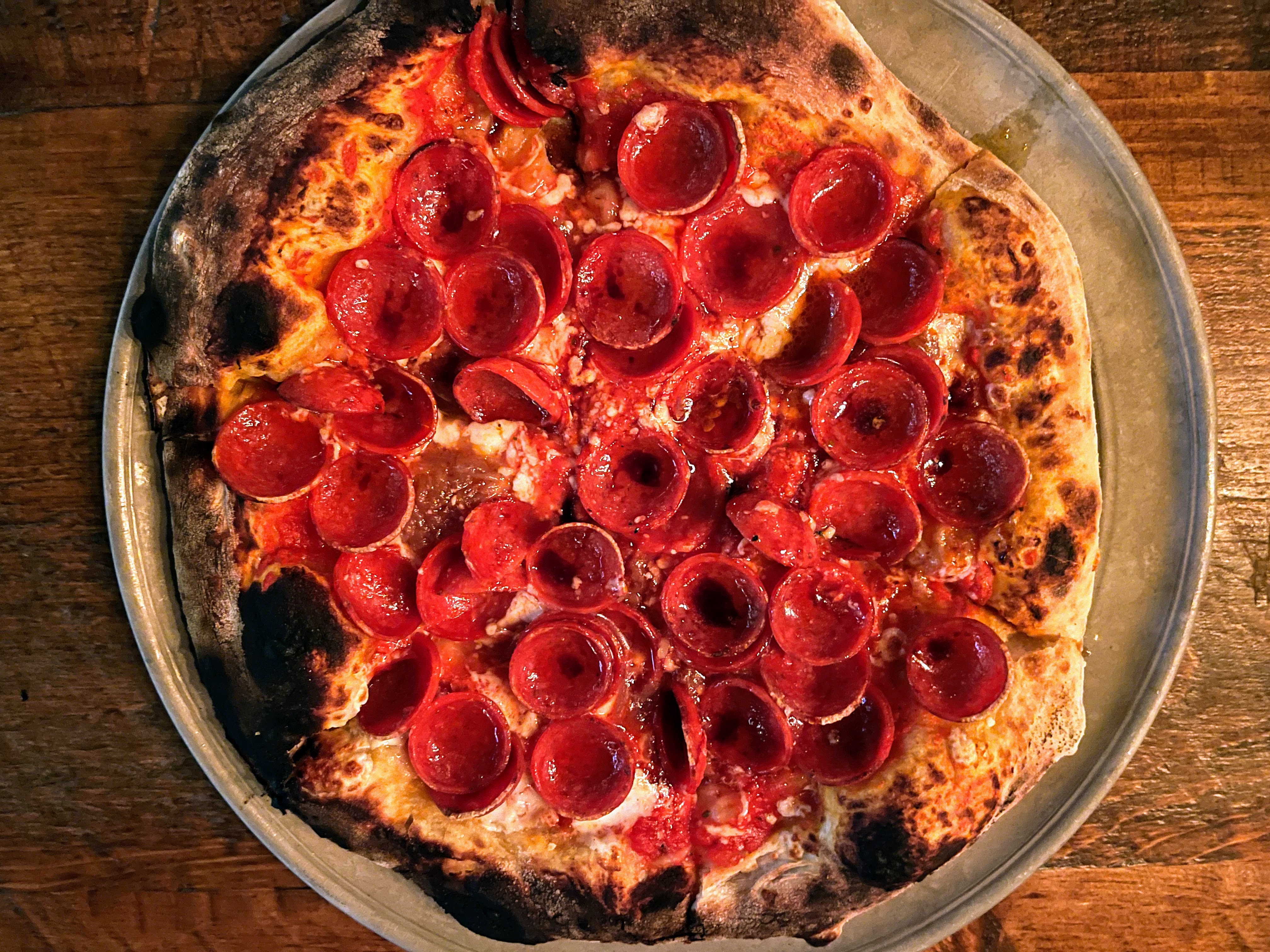 An overhead photo of a blistered Neapolitan-style pizza loaded with roni cups.