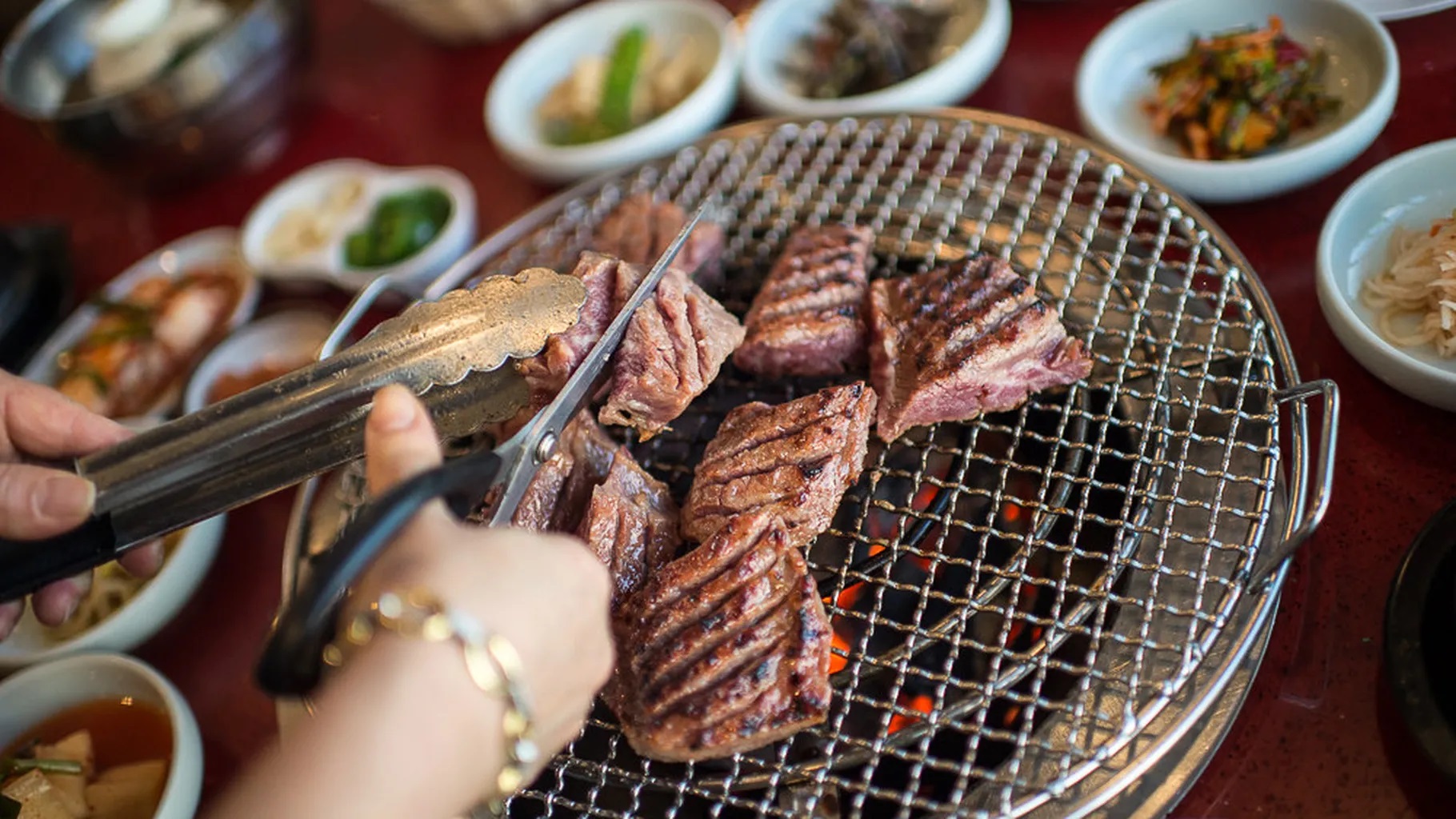 A hand with scissors cuts meat on the barbecue grill.