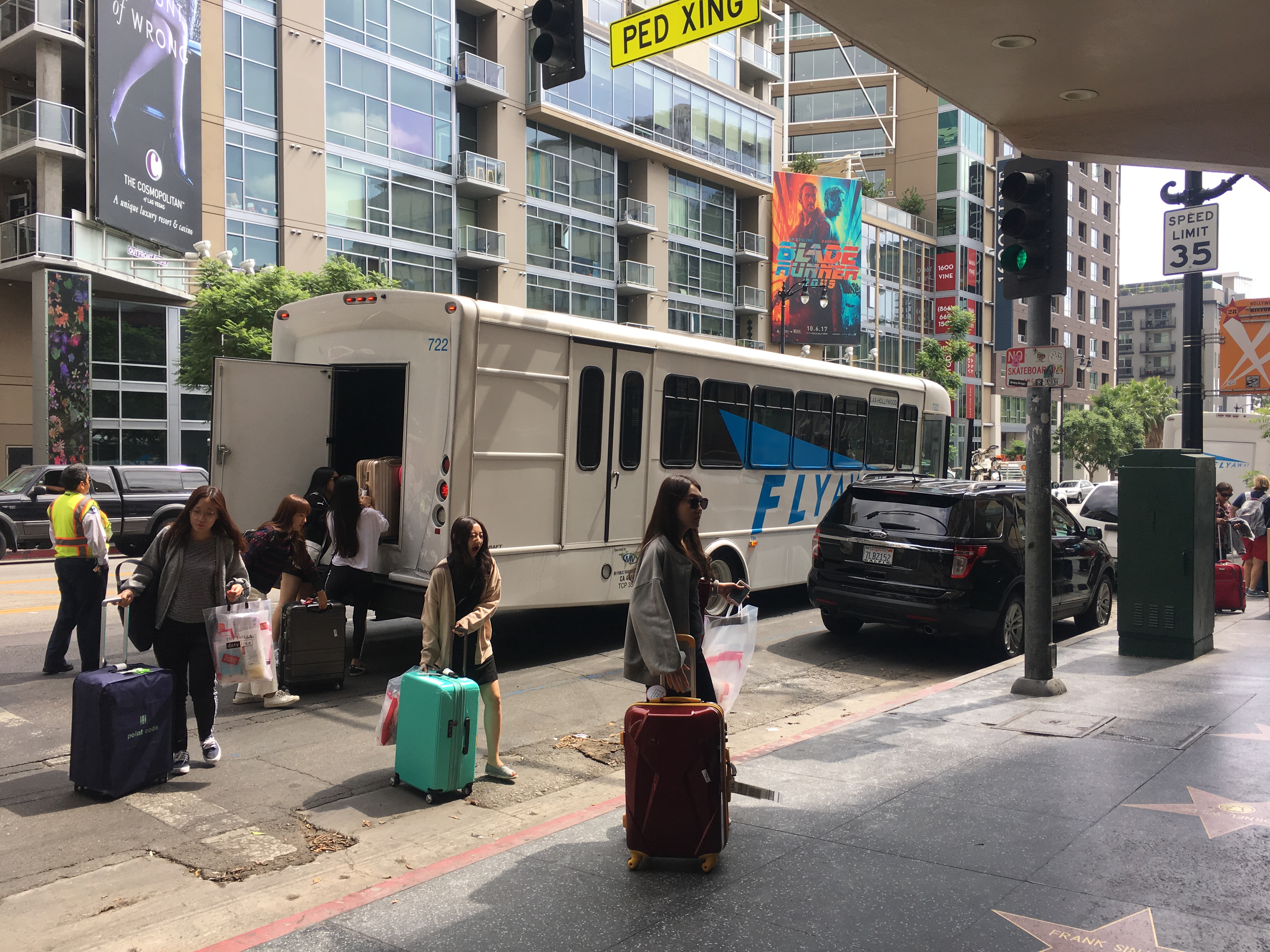 People stand next to a parked bus. Several people have luggage. 