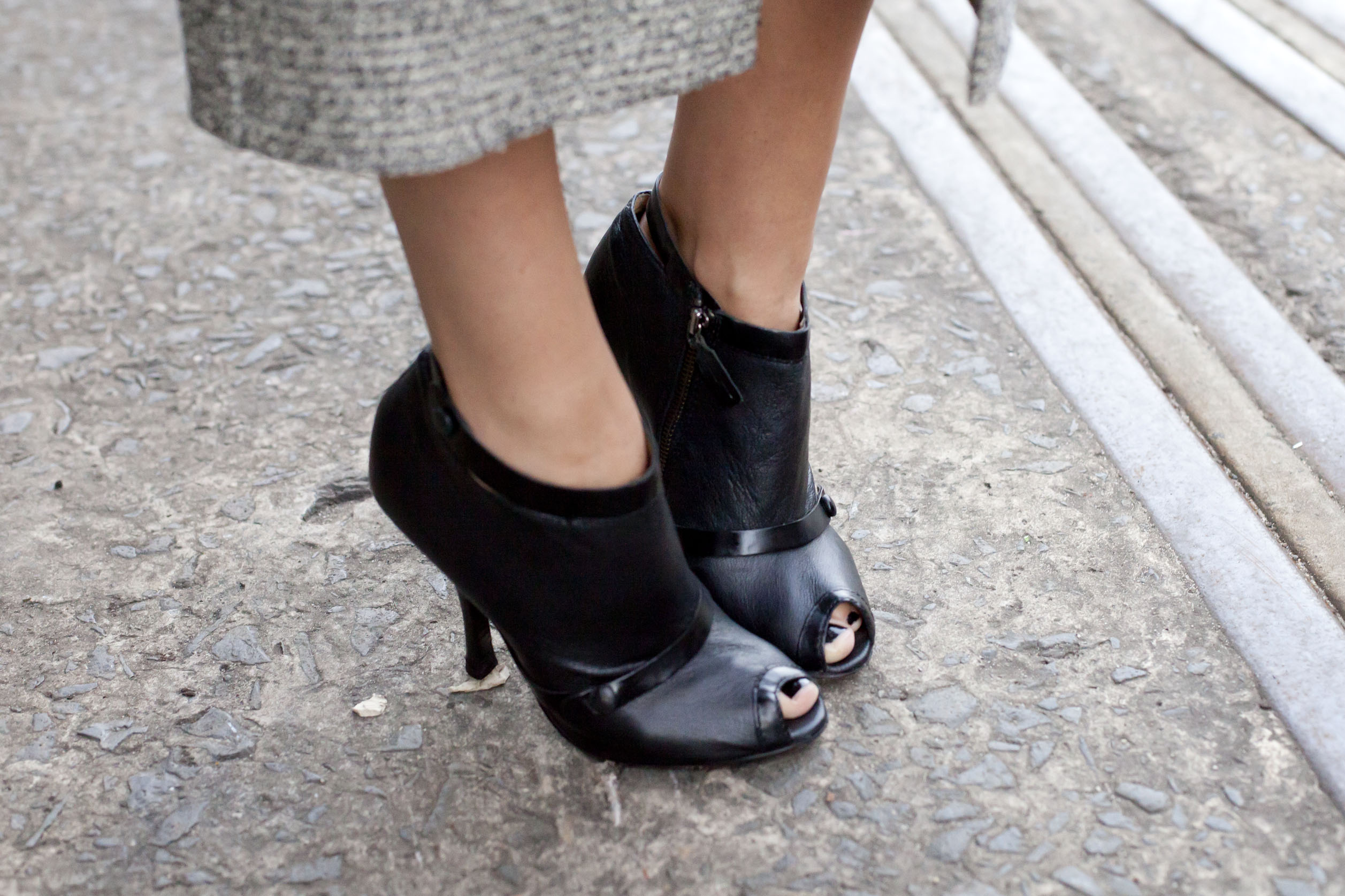 A woman from the shins down wearing black open-toe high heel boots.