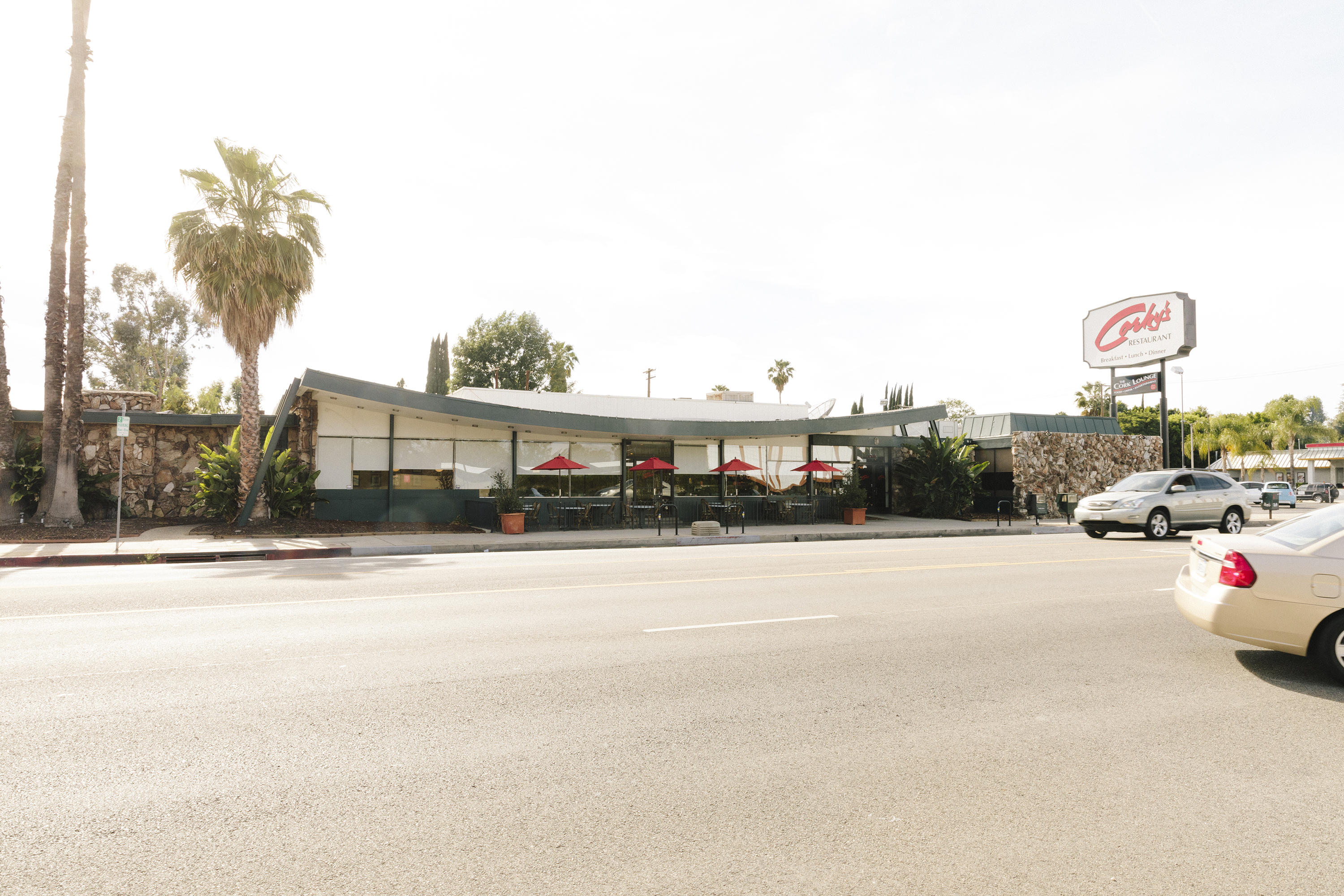 A single-story midcentury diner with a swooping long roof and a neon sign of the restaurant’s name (“Corky’s). 