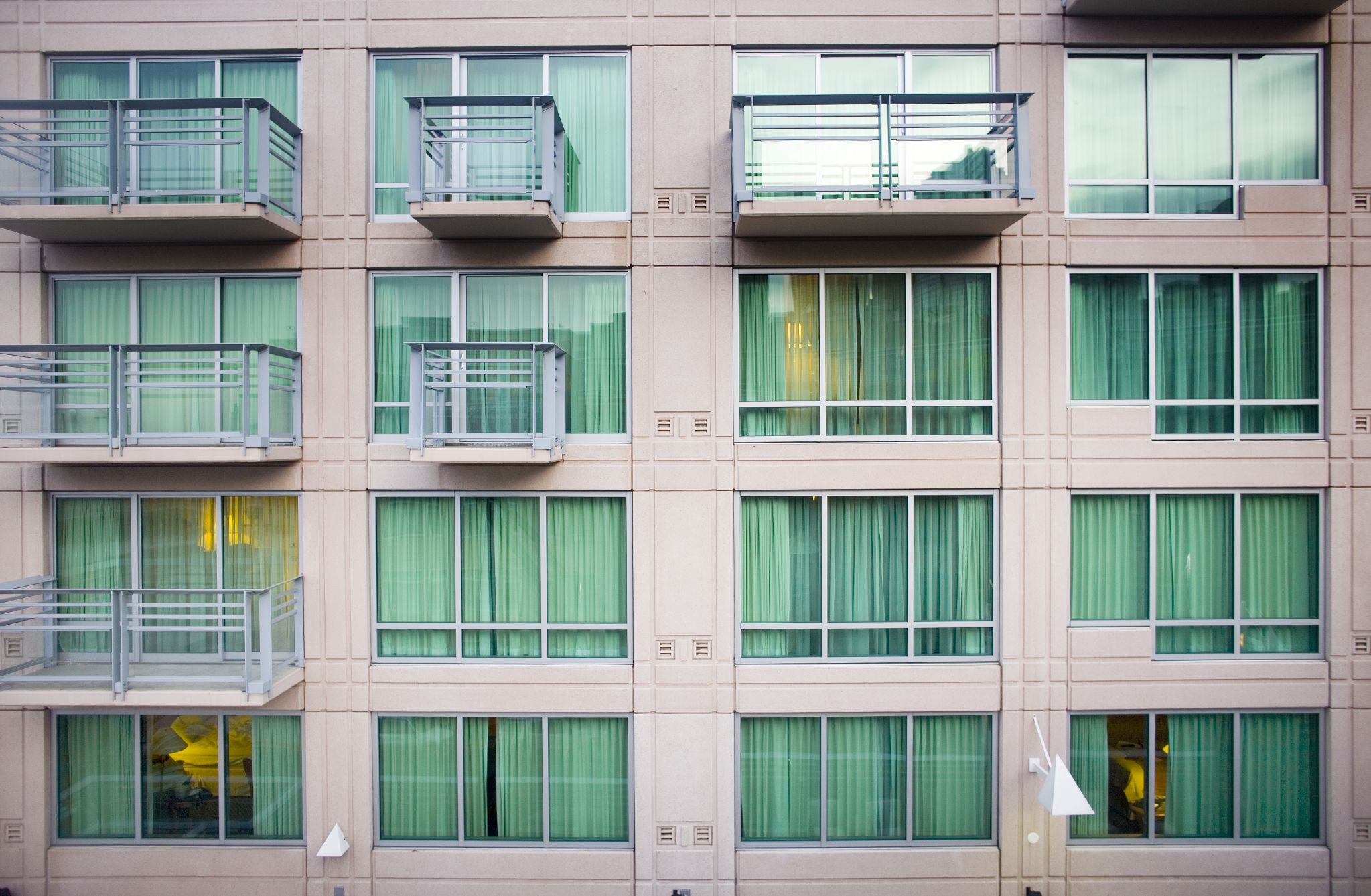 Three rows of floor to ceiling windows on the outside of a beige building with intermittent balconies.