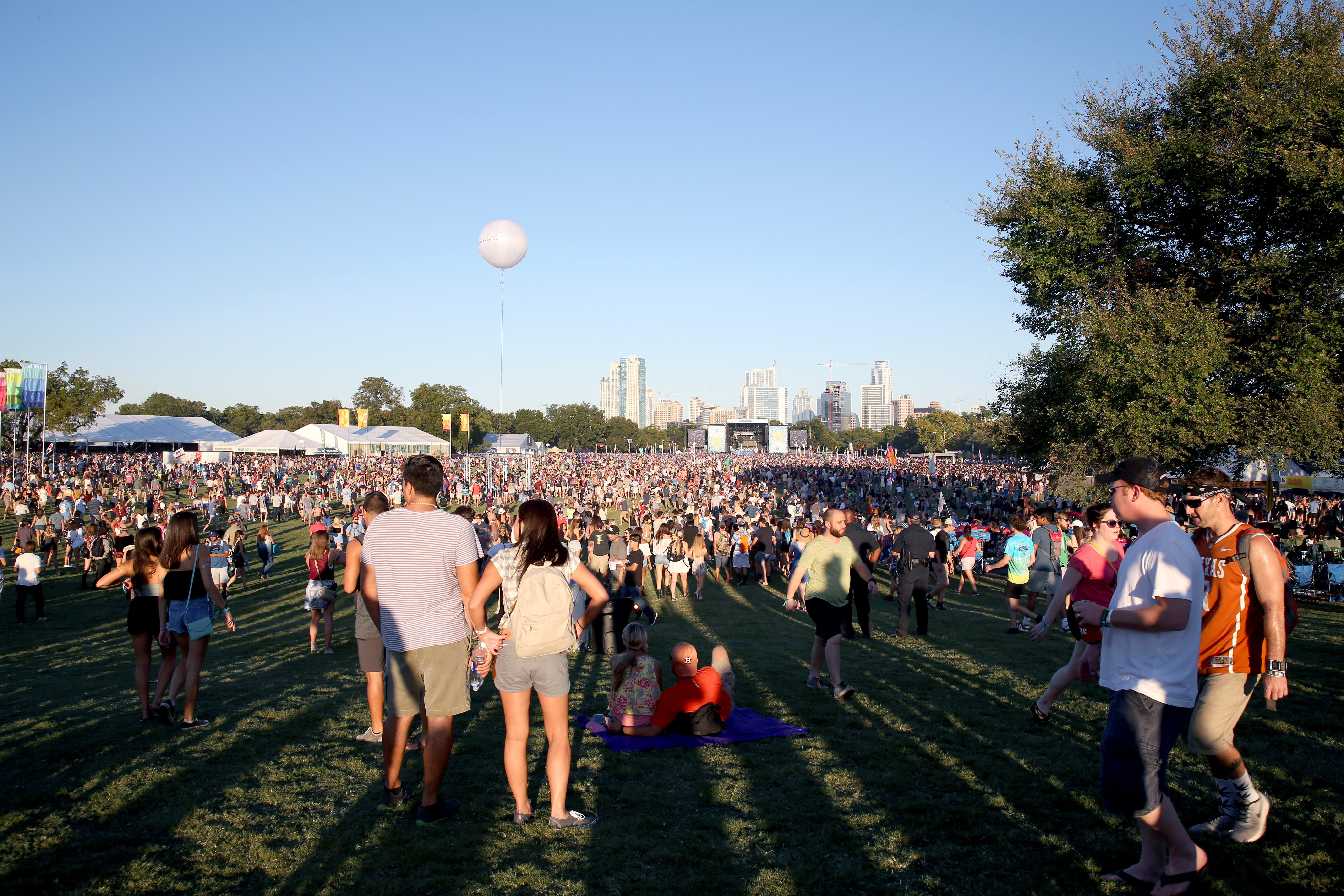 A large crowd in an Austin park with a stage in the distance, daytime