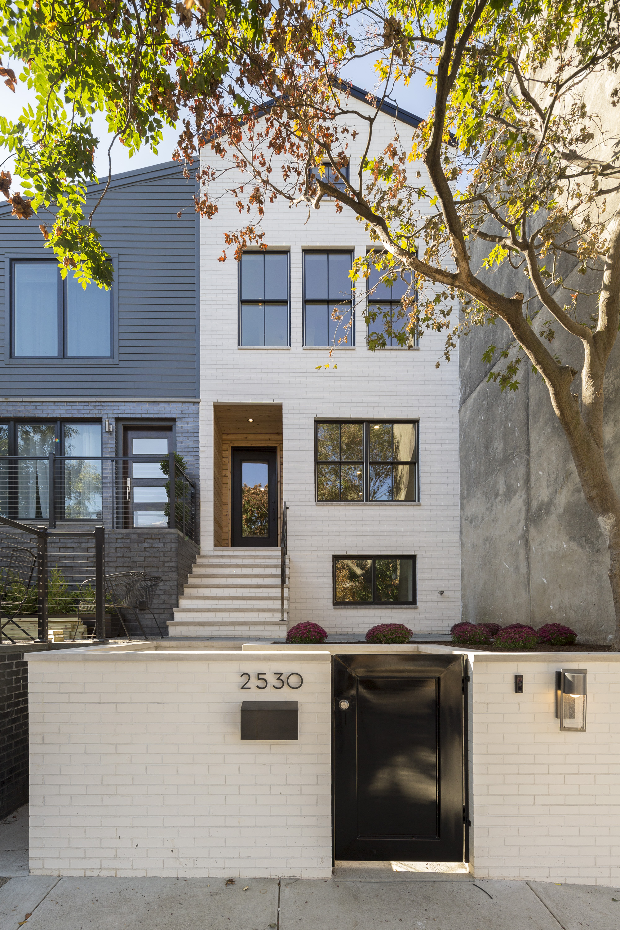 A white brick rowhome in Philadelphia’s Fitler square neighborhood with stairs leading up to a custom black door wrapped in cedar. 