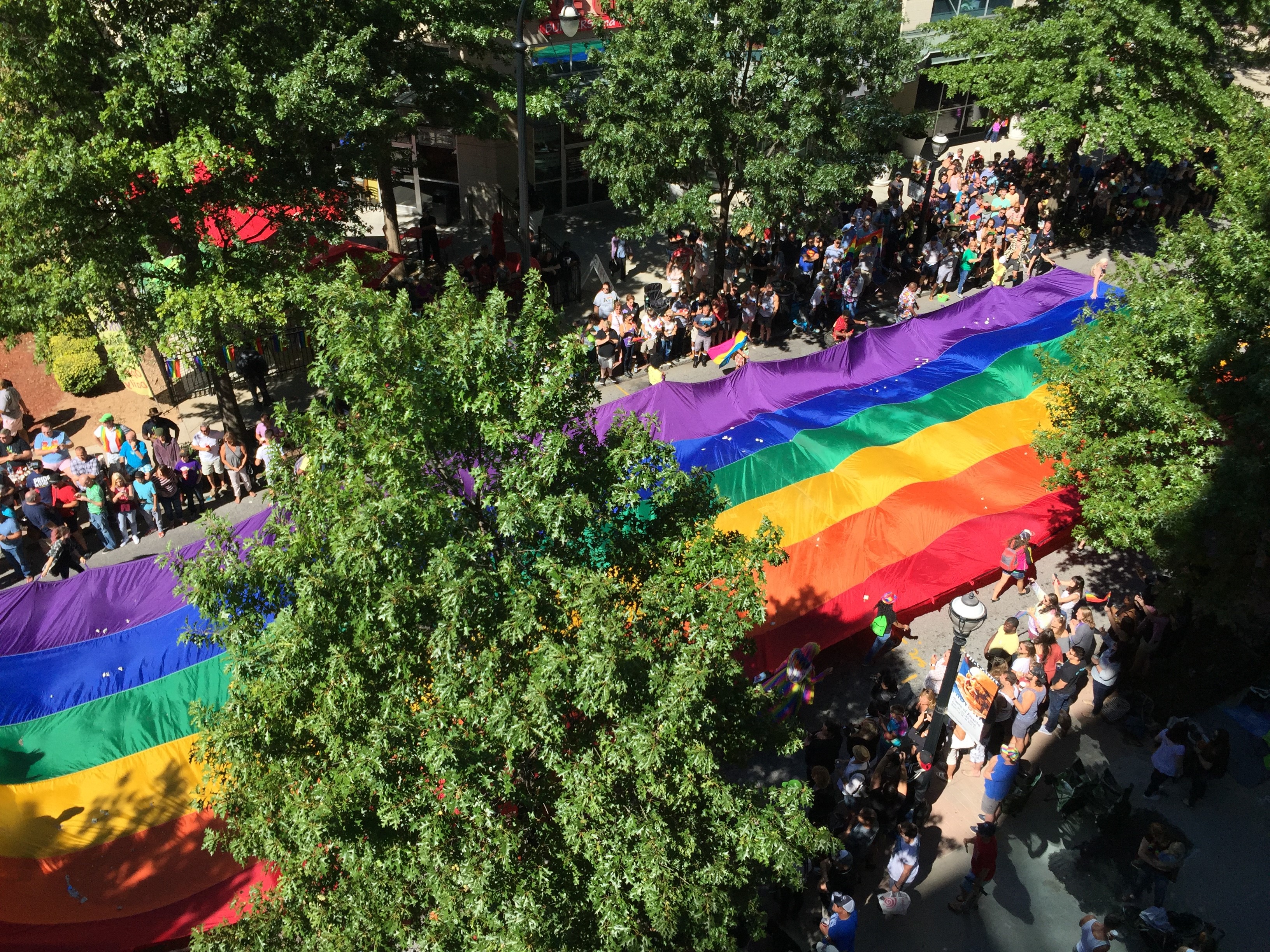 A large rainbow flag is carried down Peachtree Street in Midtown, seen from above.