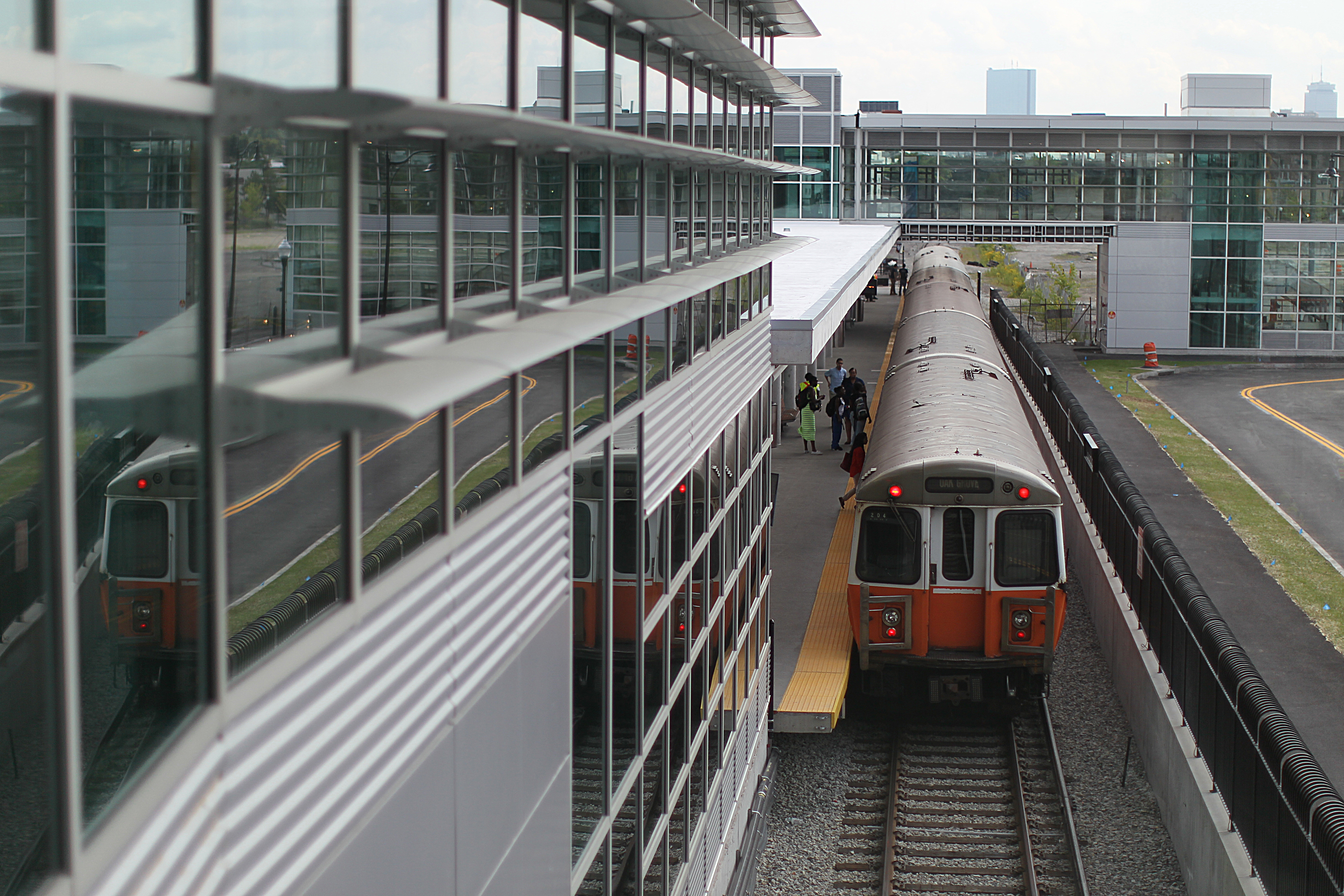 A subway train pulling away from a tall, glassy station. 