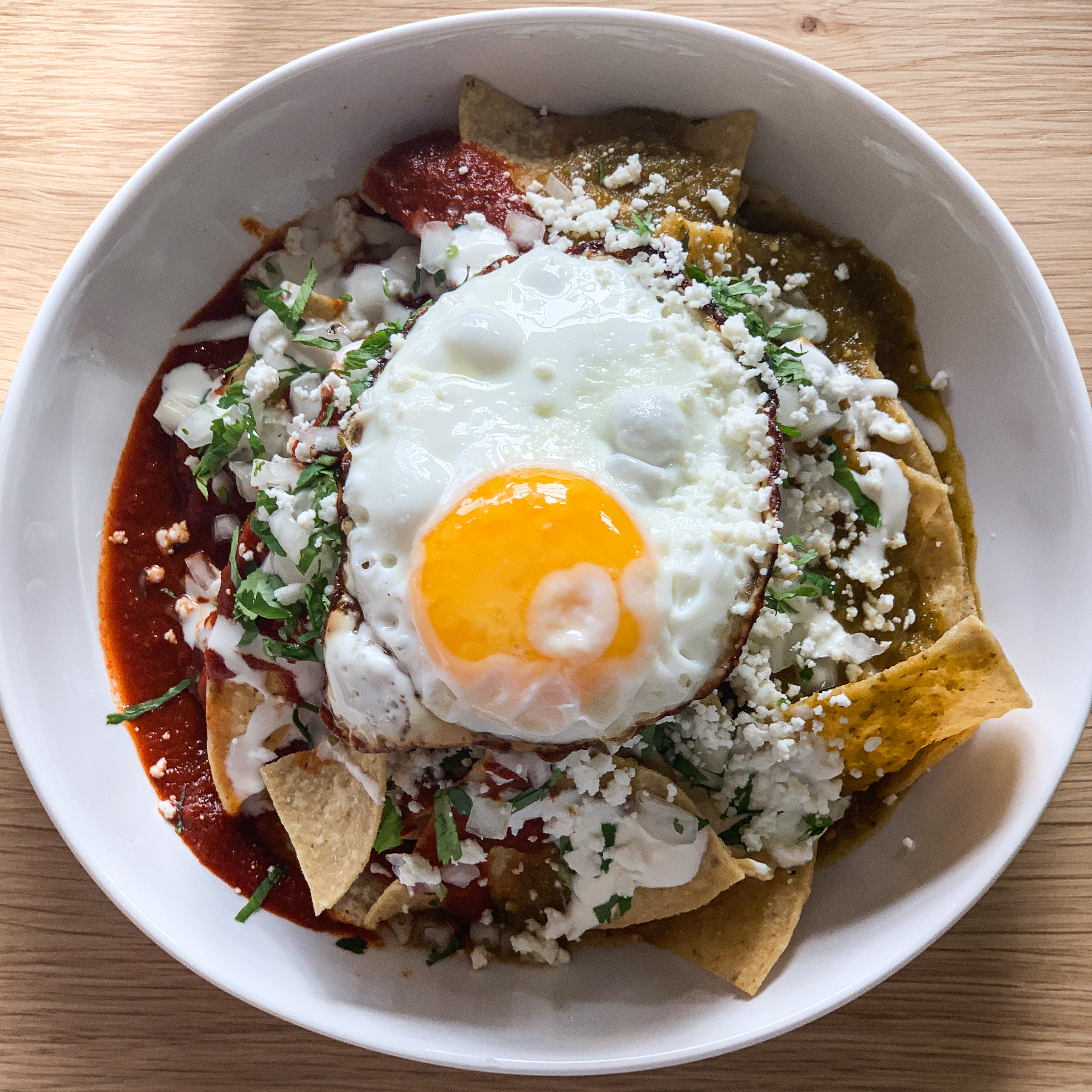 bowl with tortilla chips, cheese, red sauce, and egg