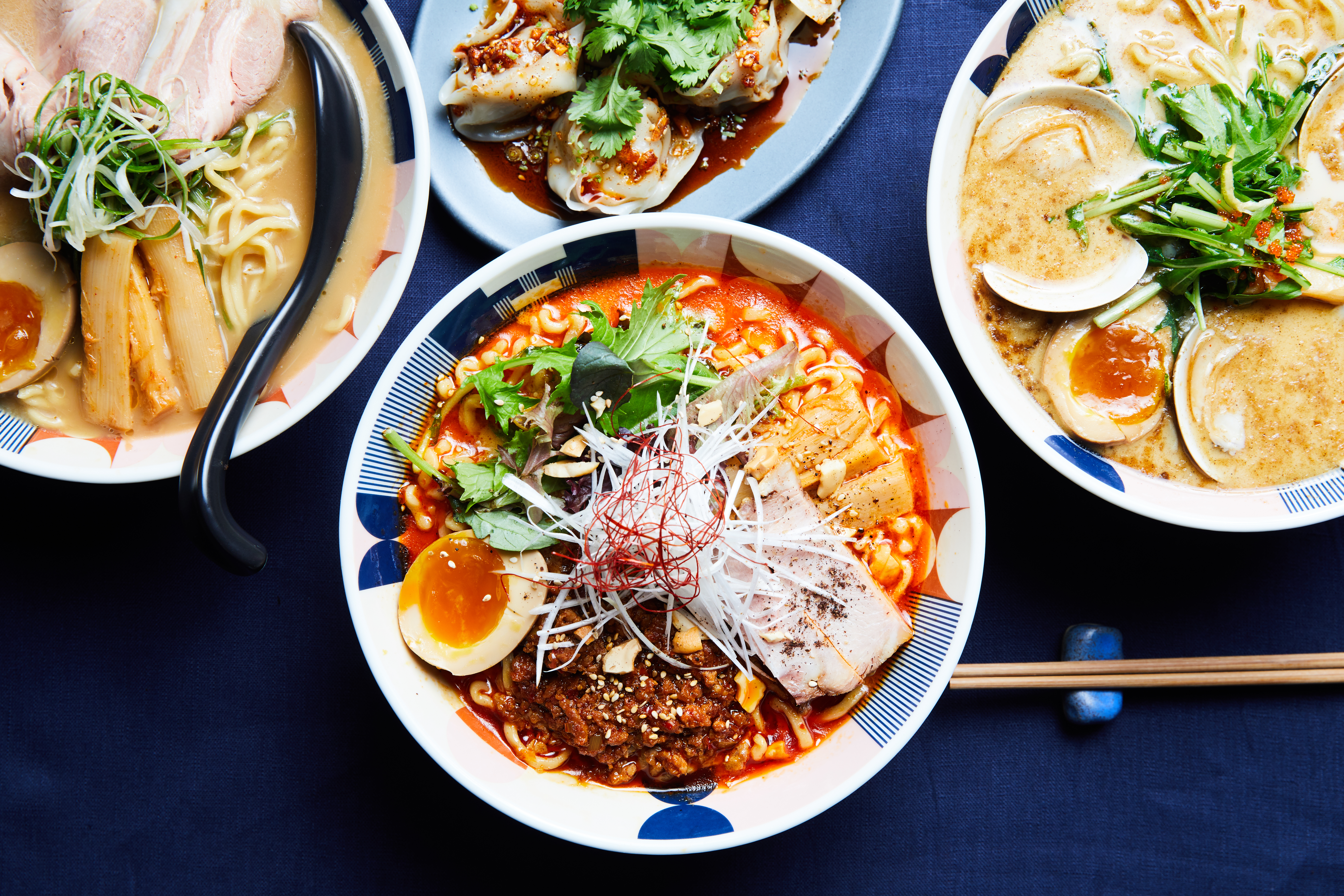 An overhead photograph of bowls of ramen on a busy table.