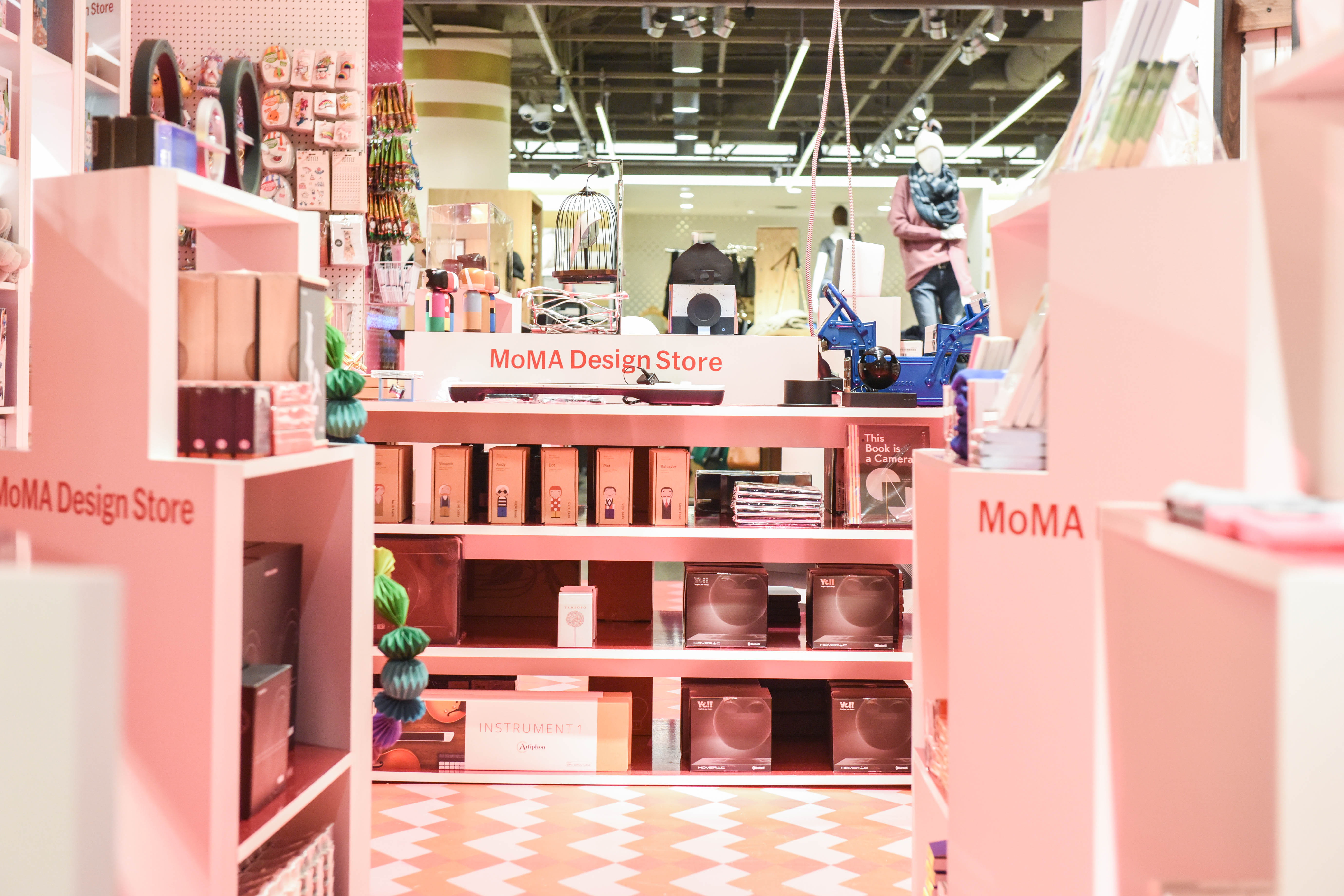 The interior of the Museum of Modern Art pop-up store at the Grove in Los Angeles. The display cases and shelves are pink and there are pink and white tiles on the floor. There are various objects on the shelves. 