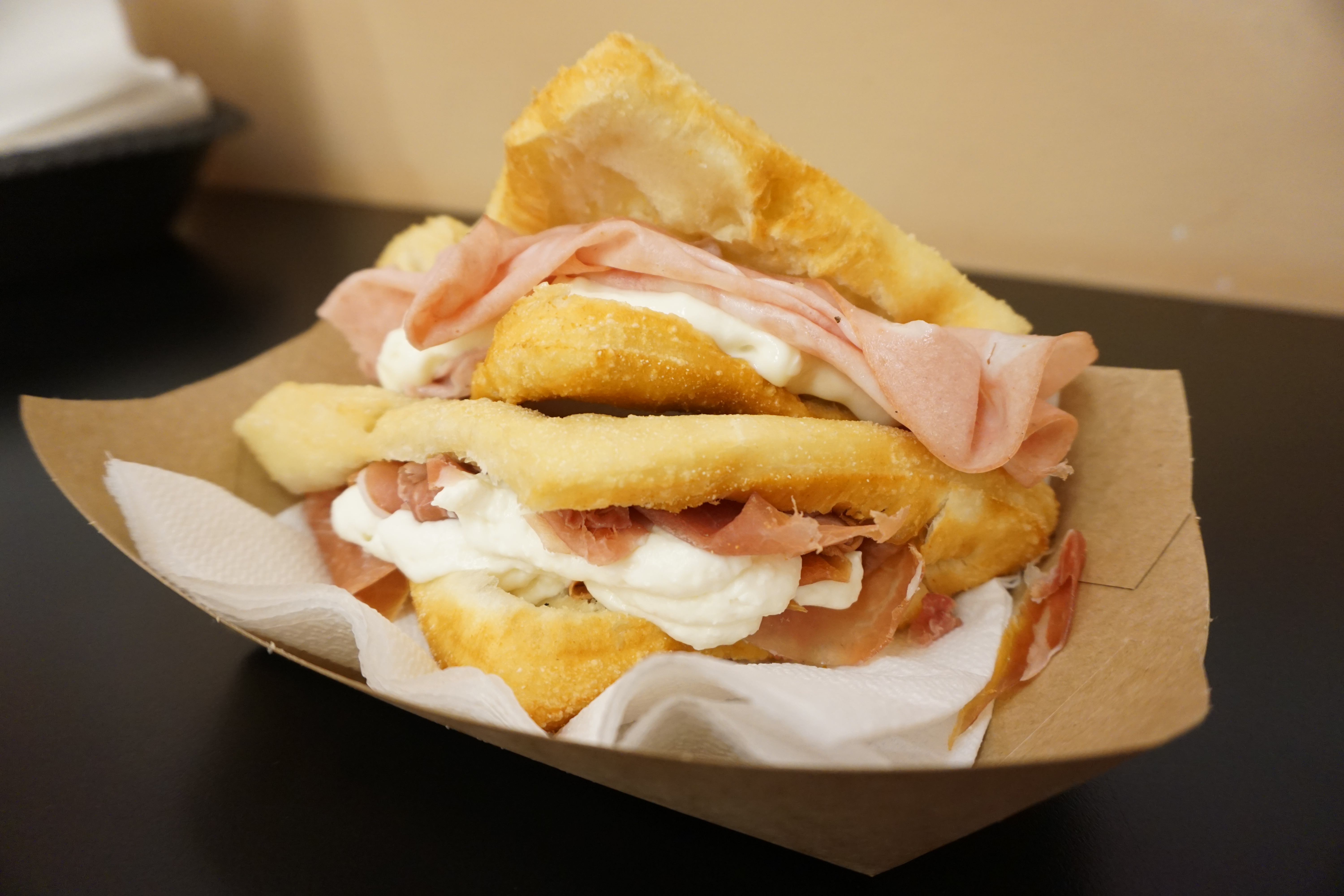 Two sandwiches stacked on top of each other with meat and cheese fillings spilling out, served in a paper boat.