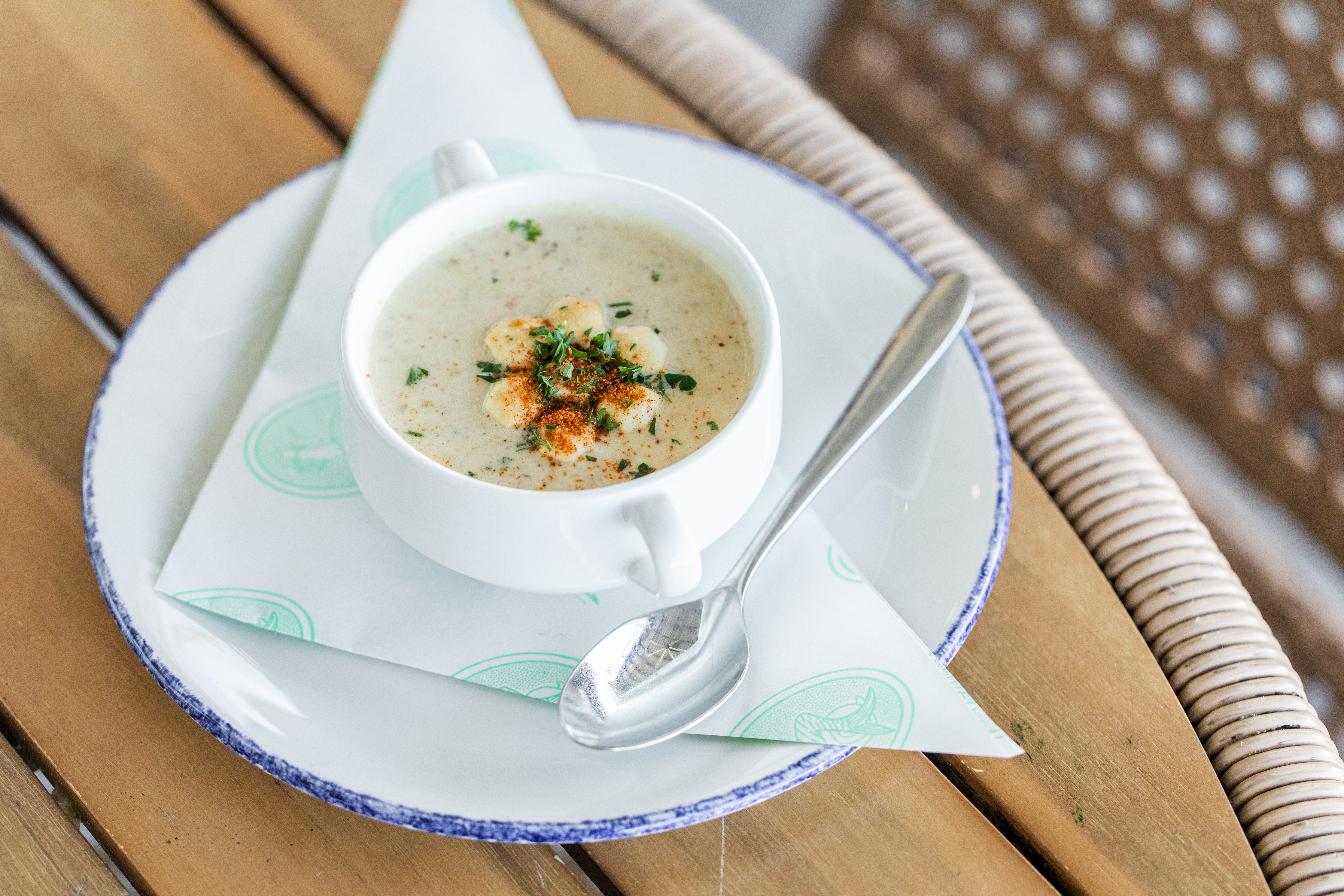 A white bowl with oyster chowder and a spoon on the side.