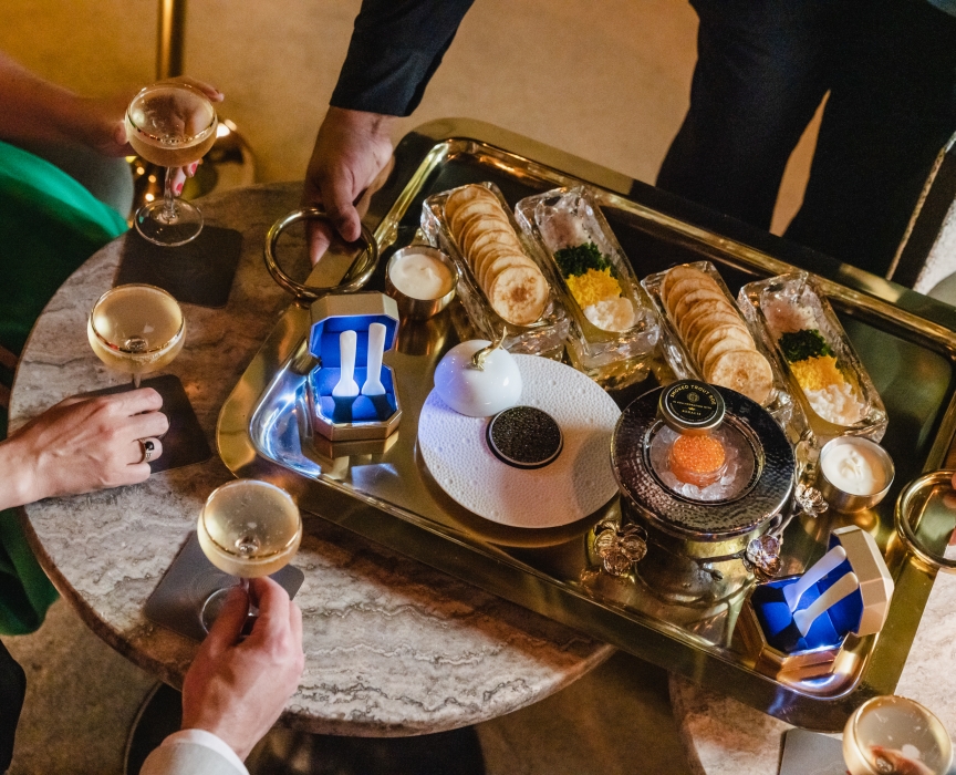A tray of caviar and crackers plus people holding coupes of Champagne.
