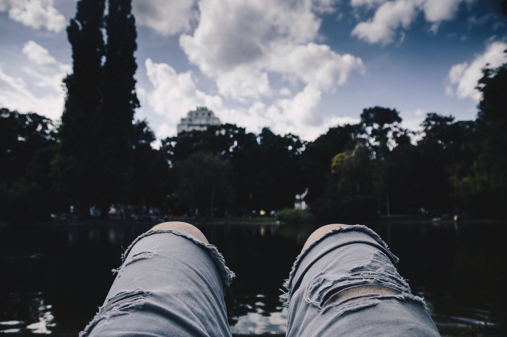 A pair of legs in ripped jeans looking up at trees and the sky