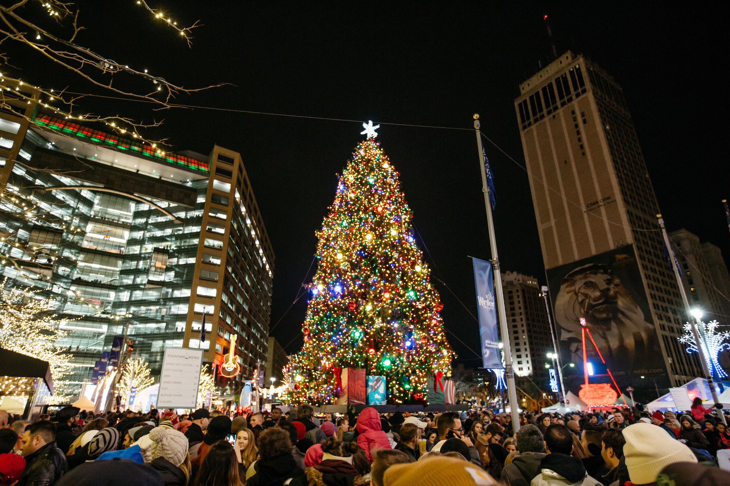 A huge Christmas lit up at night in Campus Martius Park is surrounded by people.