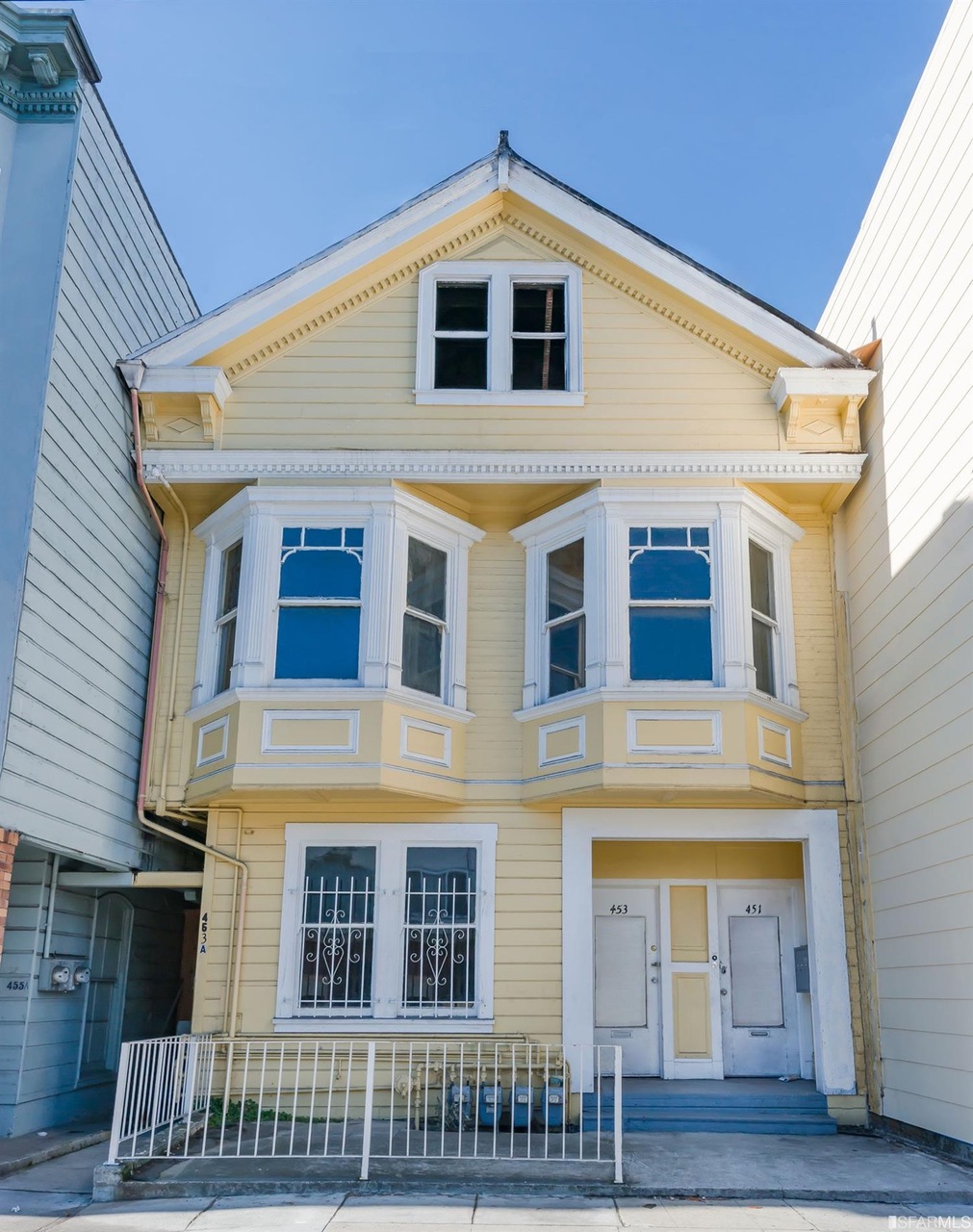 The undamaged looking facade of a yellow Richmond district Victorian home.