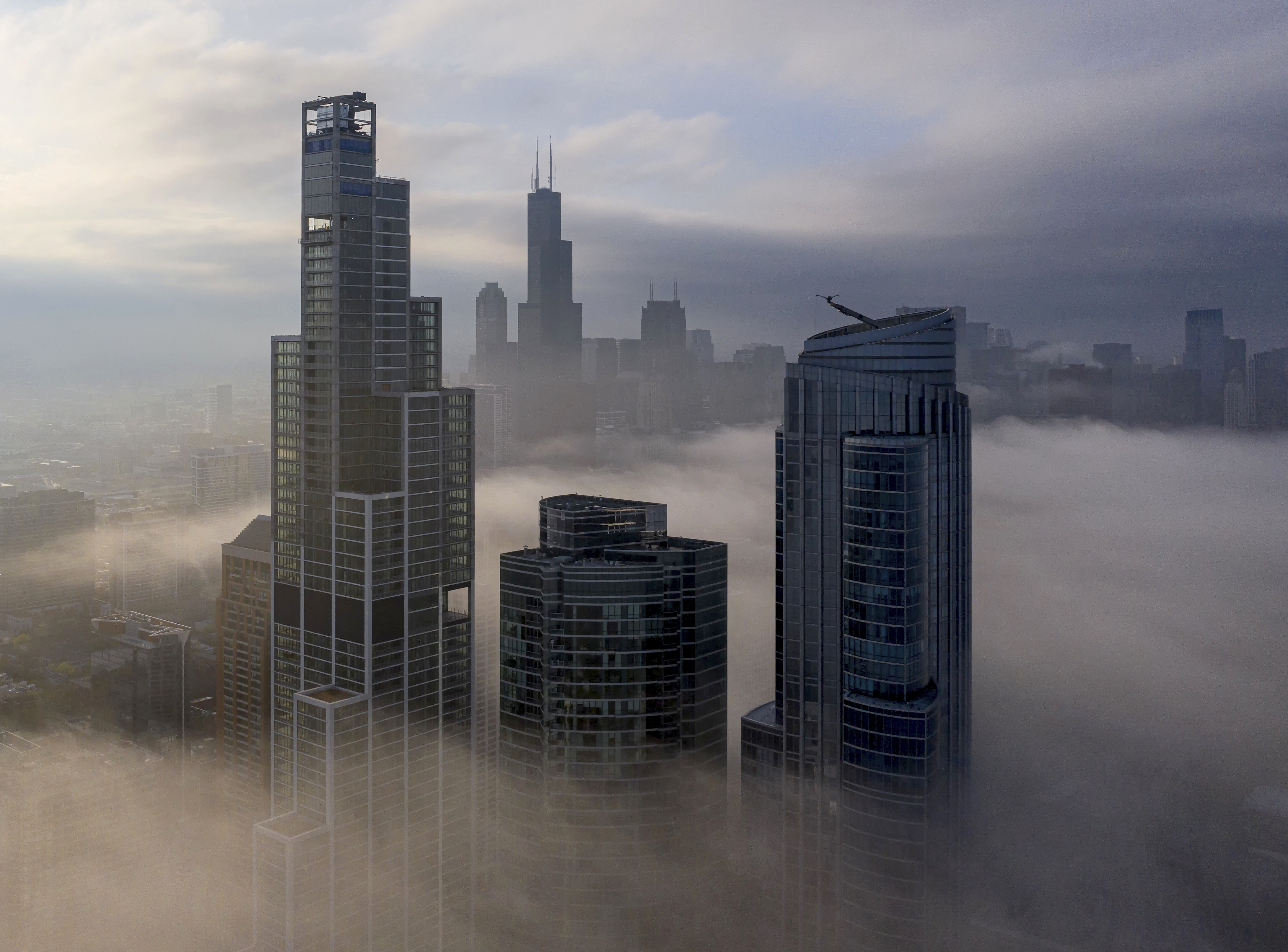 Several high-rise buildings poke through a lawyer of low fog hovering over a dense city. 