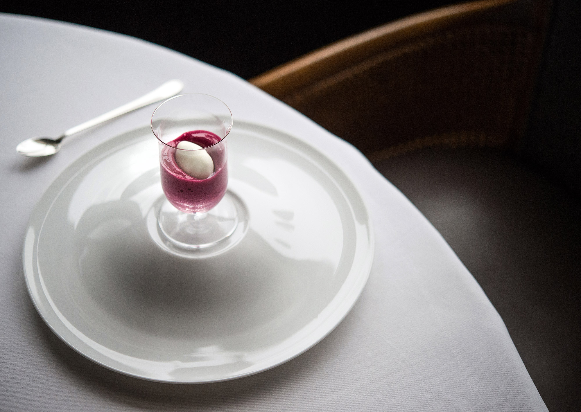 A purple-colored foam sits underneath a white quenelle in a clear glass on a white plate at Per Se