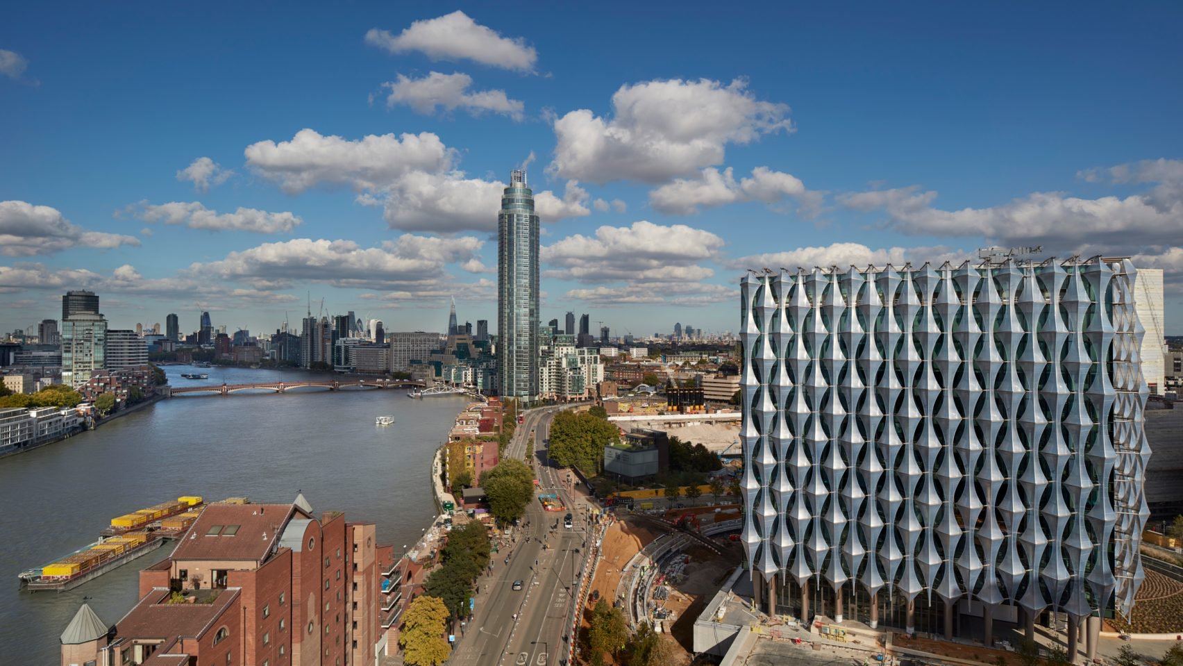 Cuboid glass building sheathed in faceted solar shading panels rises by the river in London.
