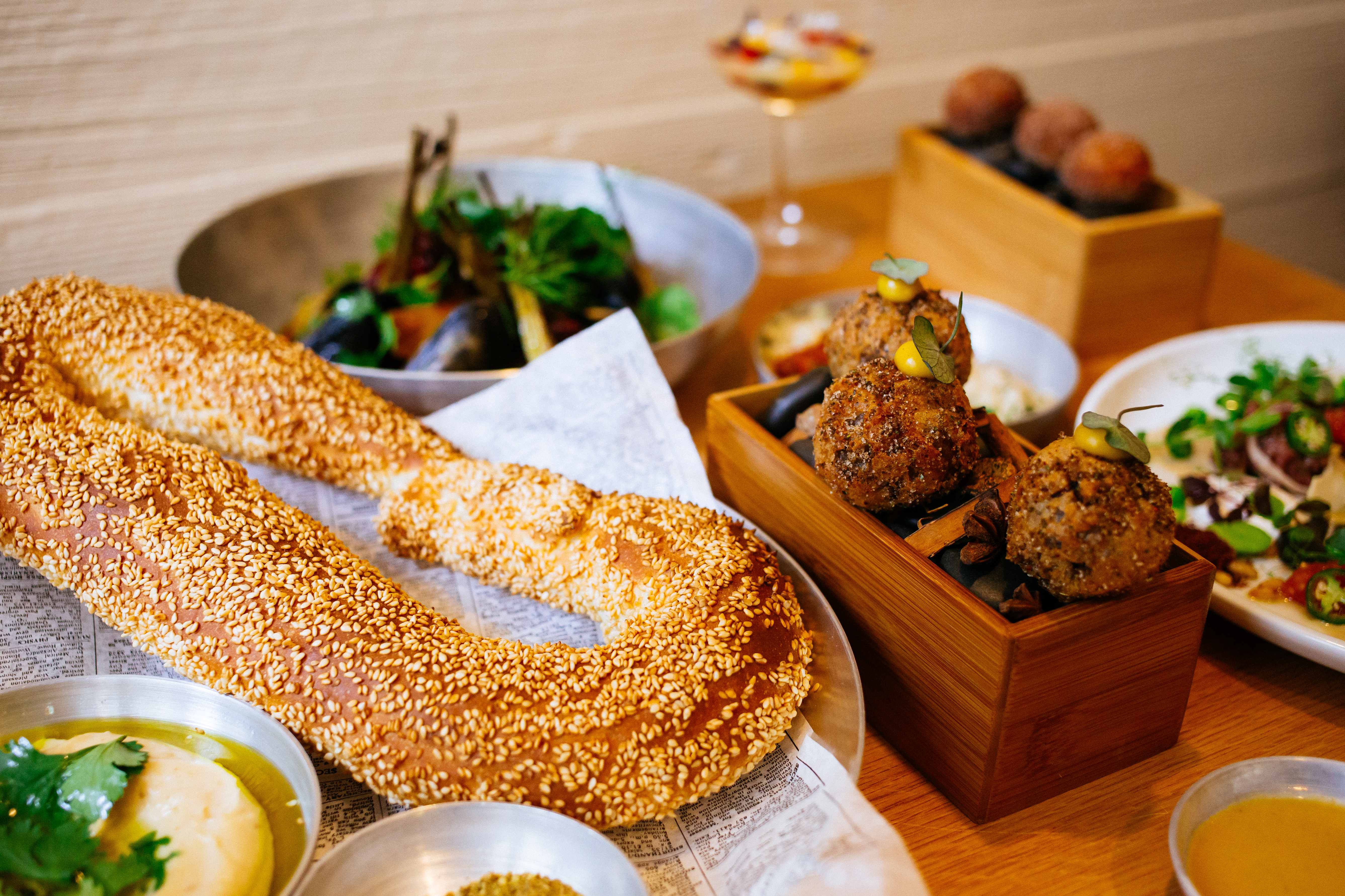 A spread of food from Nur, including a sesame-studded bread product and round balls on wooden boxes.