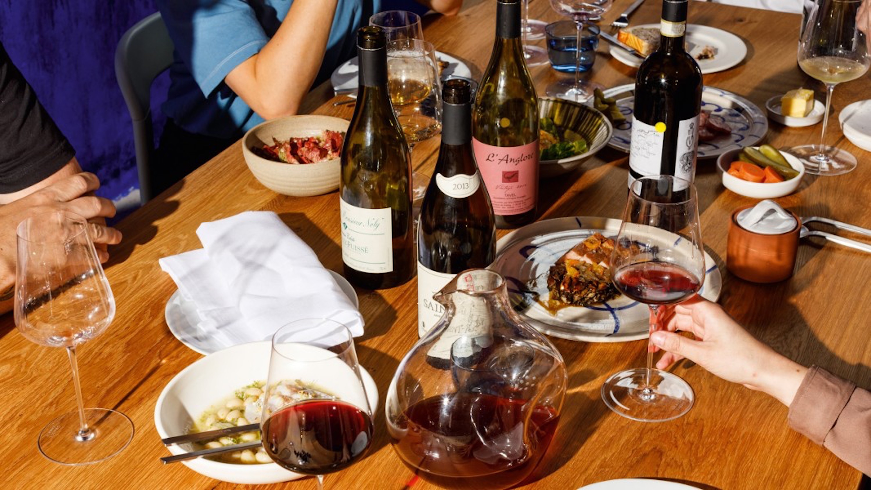 A selection of wines and French dishes in white dinnerware on a mid-century table.