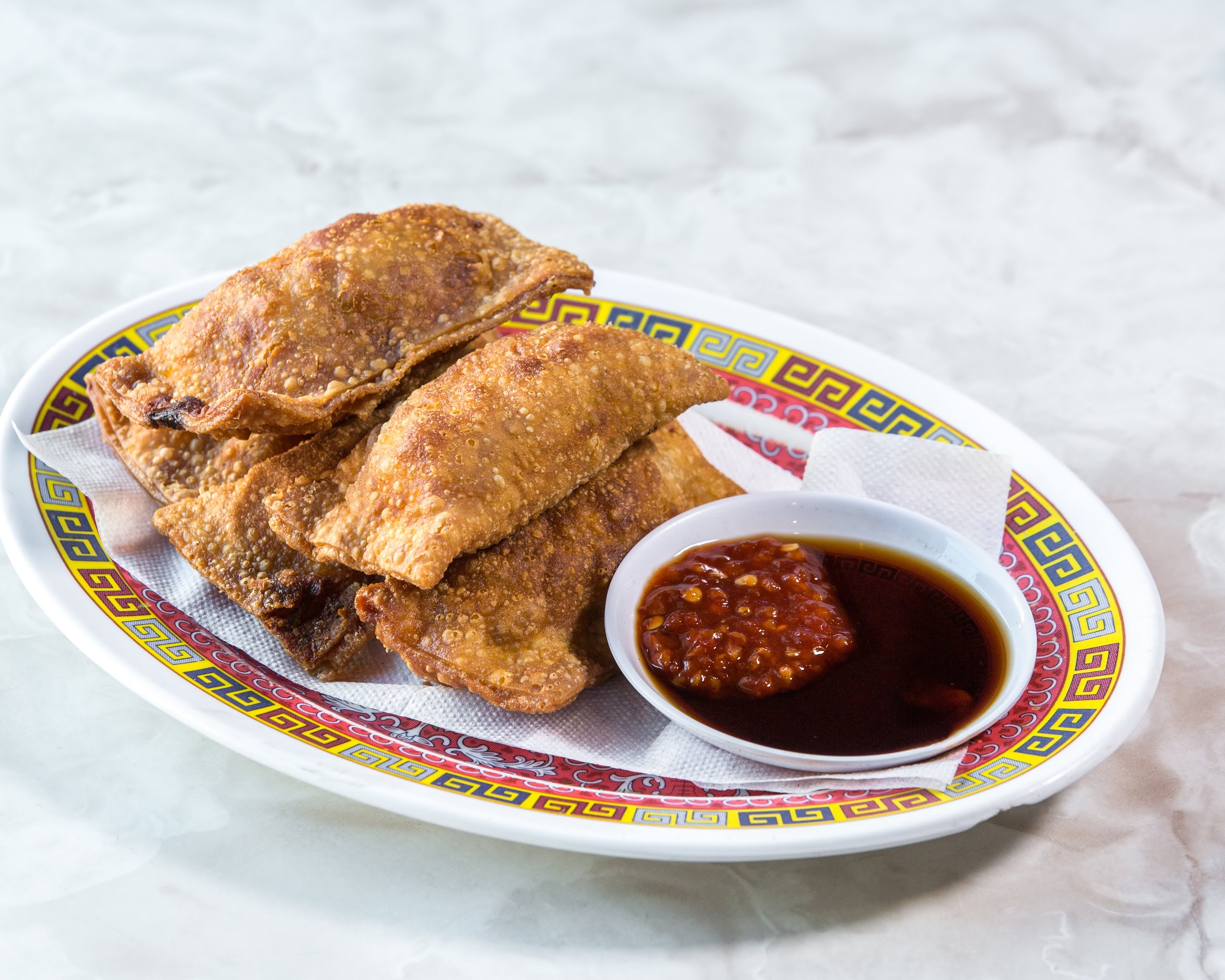 Fried dumplings on a decorative plate with dipping sauce