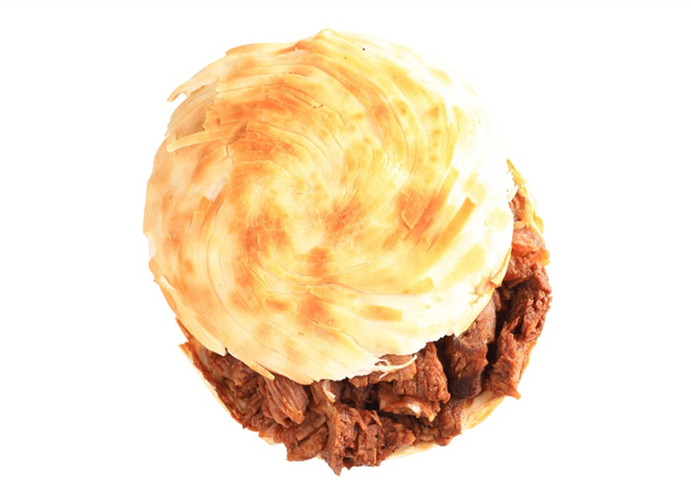 A rougamo, or Chinese “burger,” sits on a white background, with meat visible between two pieces of flatbread