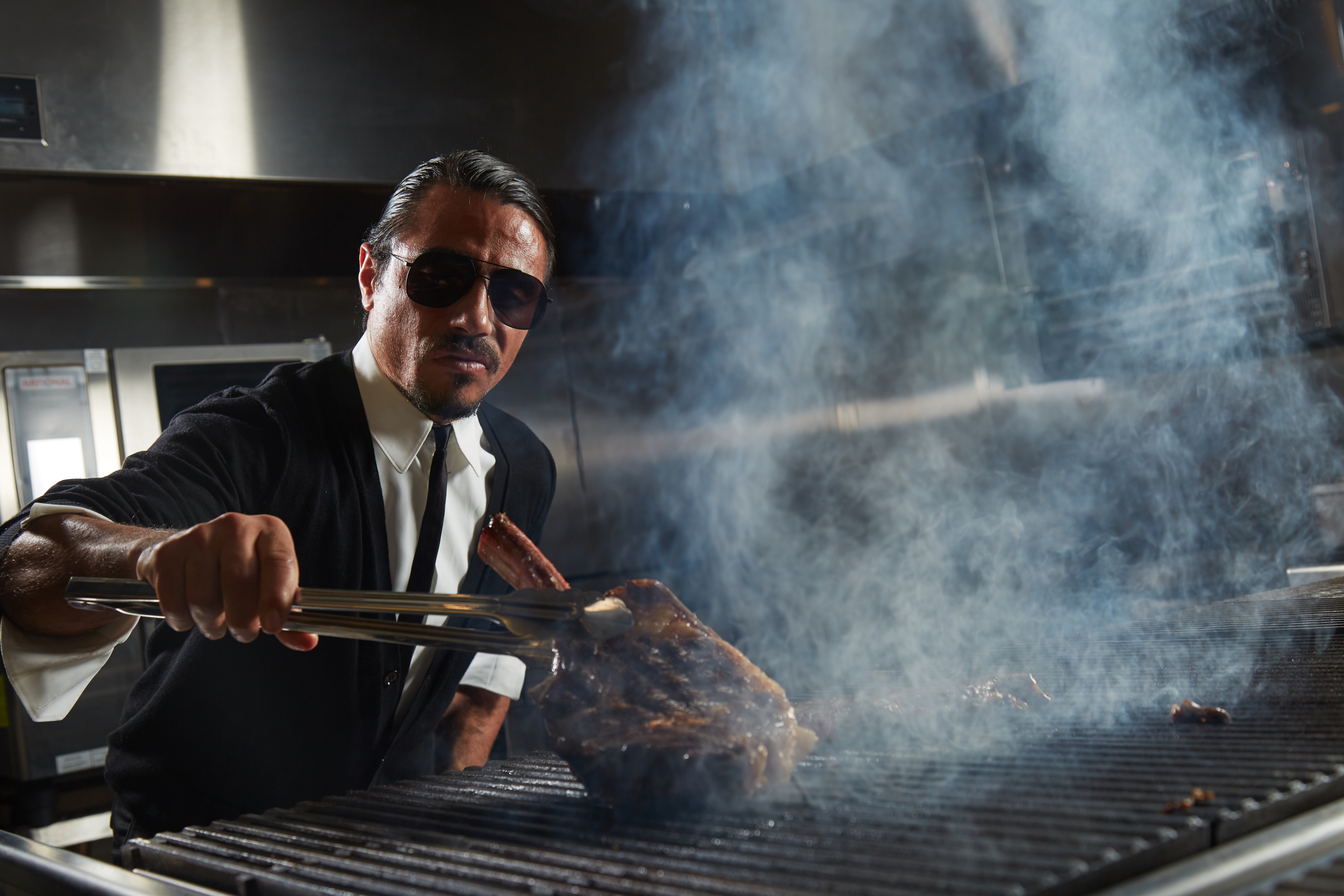 Salt Bae, standing over a grill, wielding a tomahawk steak.