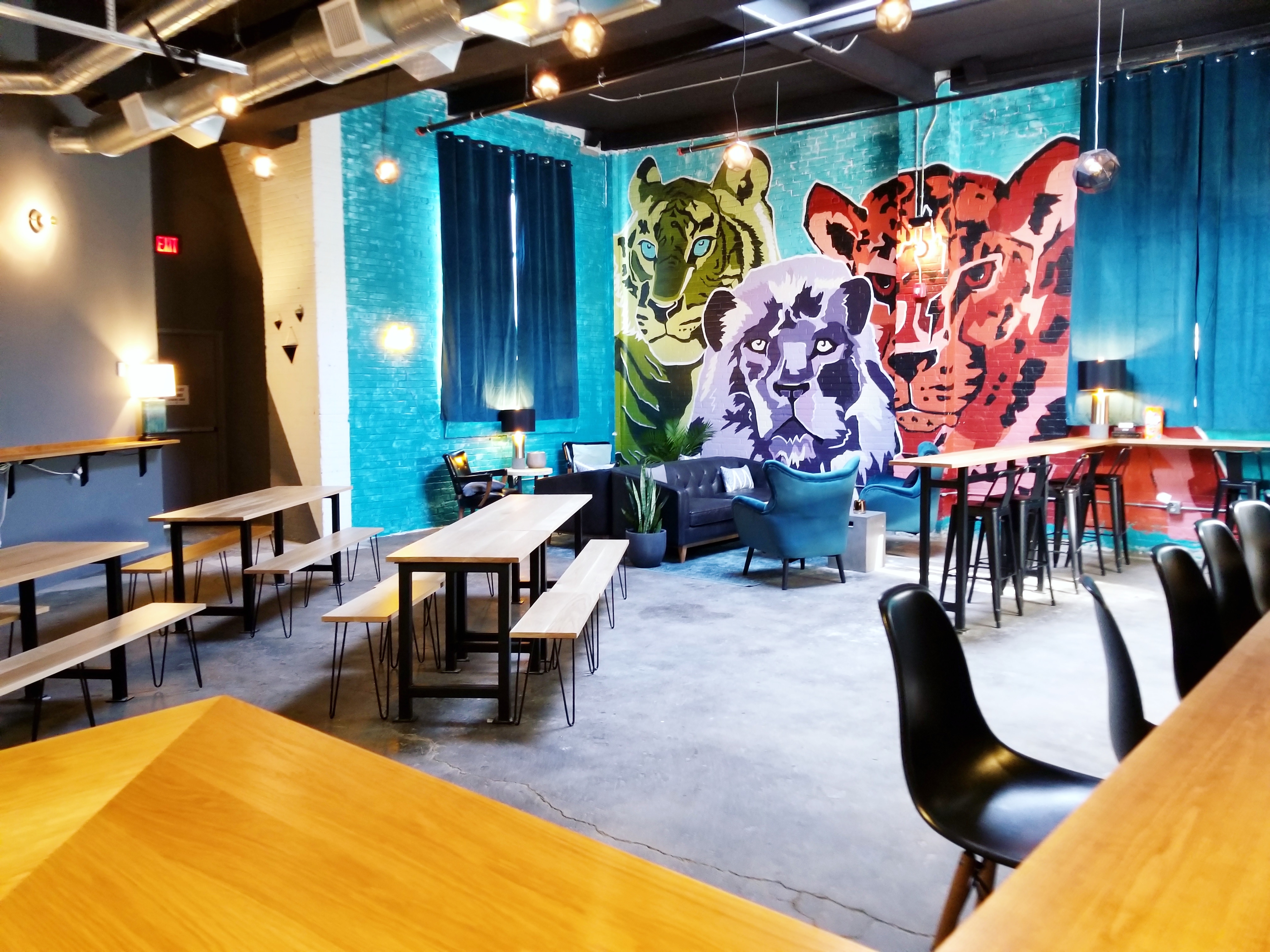 Wide view of a taproom with a mural of big, wild cats, bench seating, and bar seating